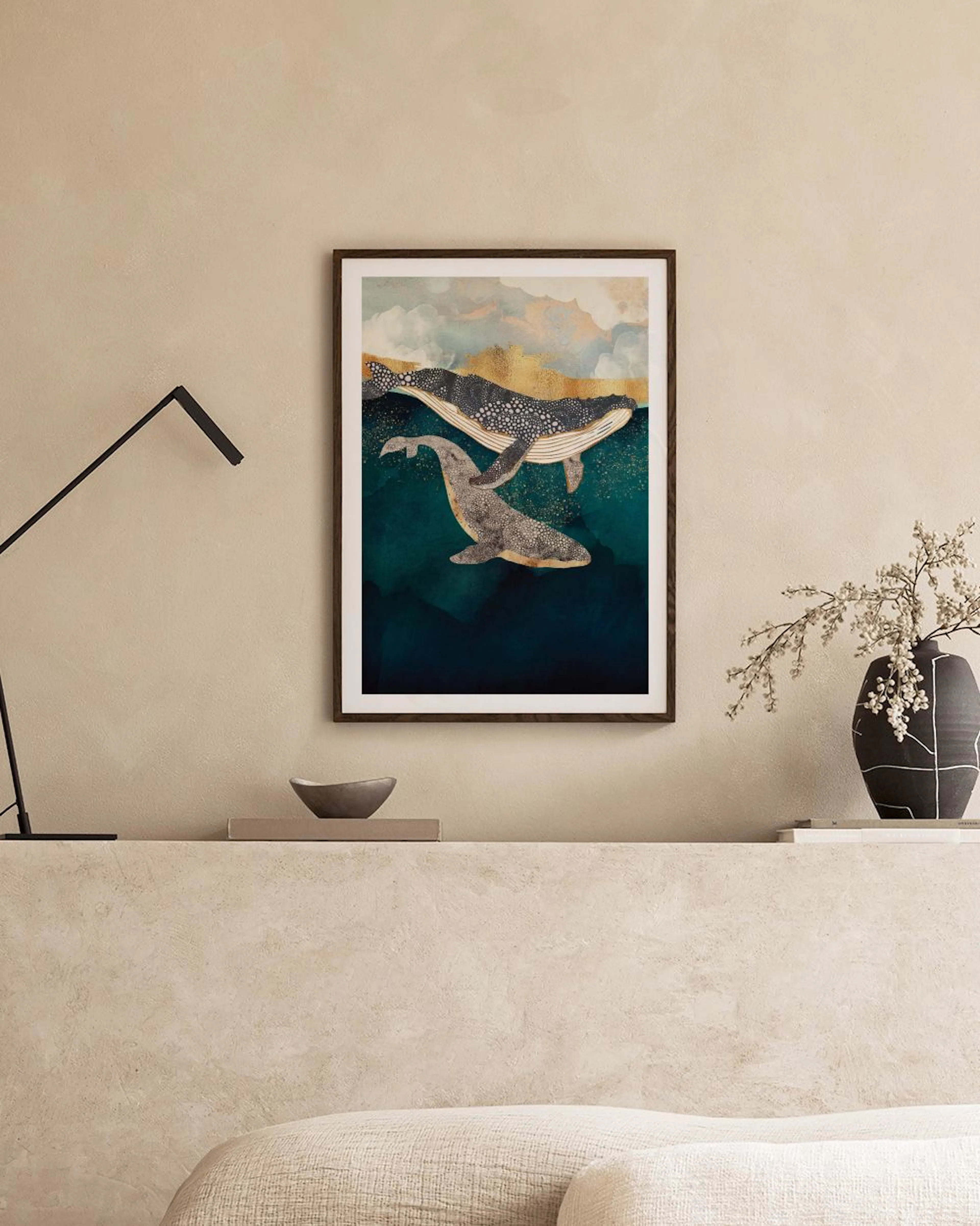 Plakat med to hvaler i turkisblåt vand, hængende over et hvidt natbord med en lampe og en tromme.