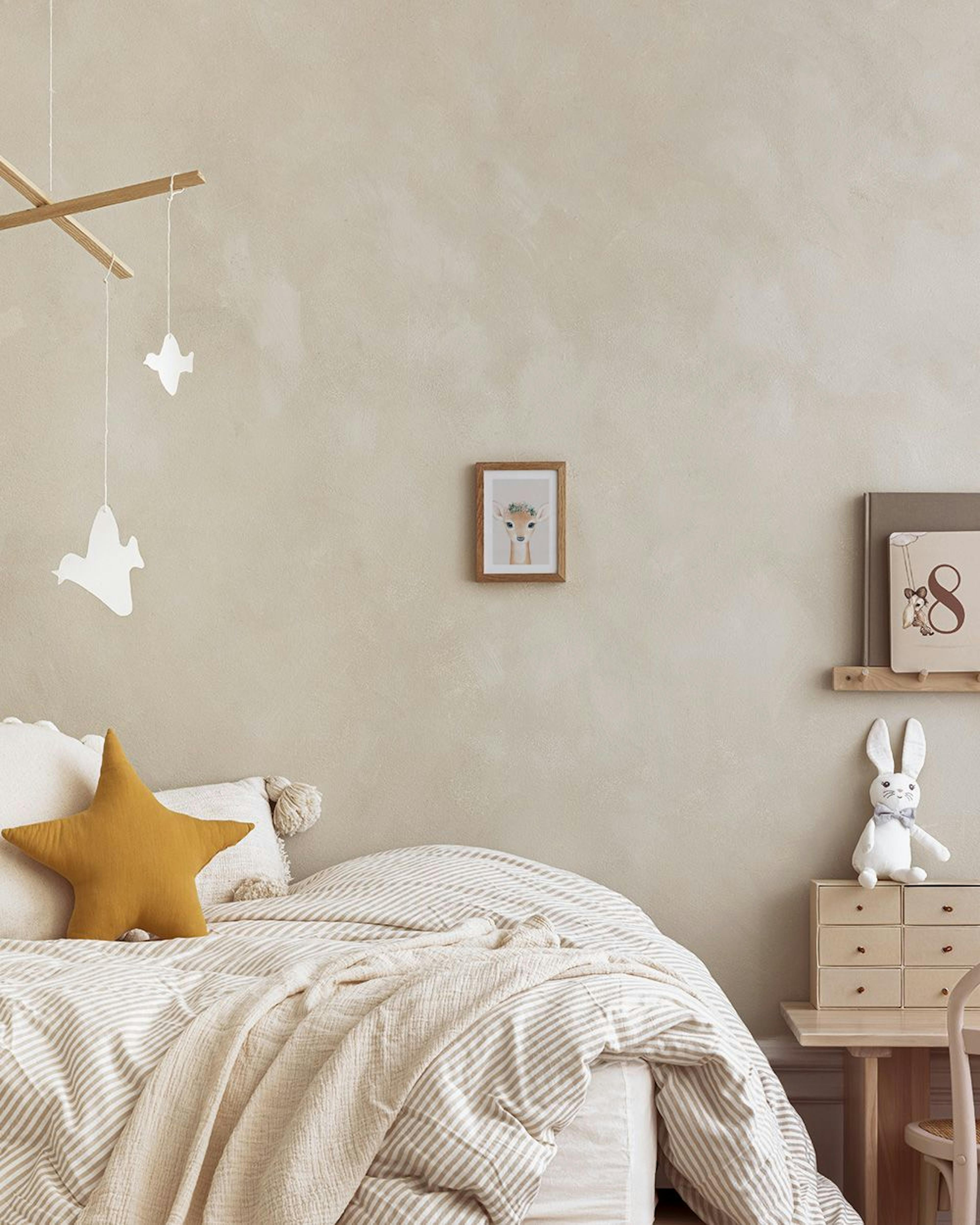 Plakat med en sød fawn med blå øjne og blomsterkrans, hængende over et hvidt natbord med en lampe og tromme.