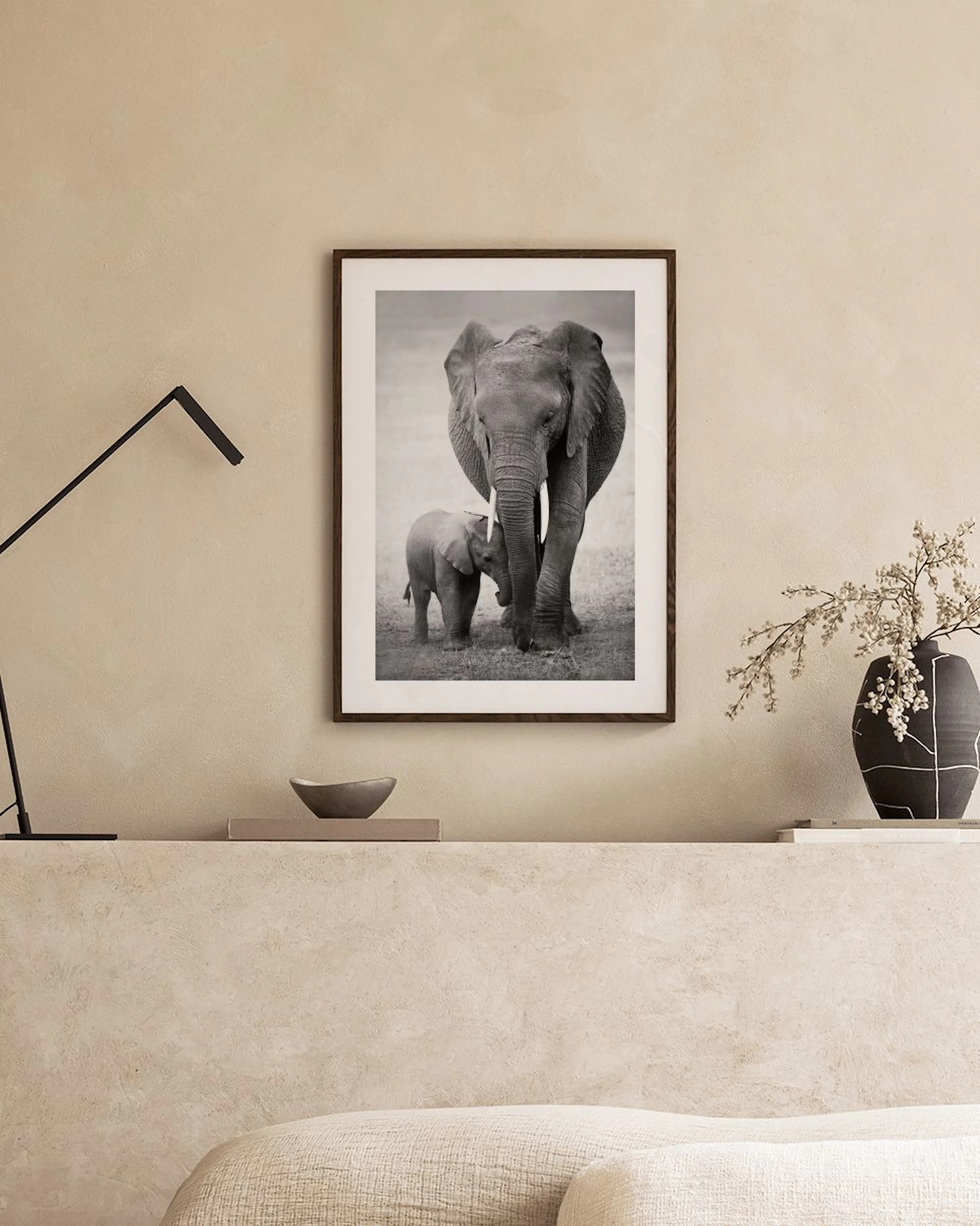 Zwart-wit poster van een olifantenkalfje naast zijn moeder, hangend boven een wit dressoir met decoratie.