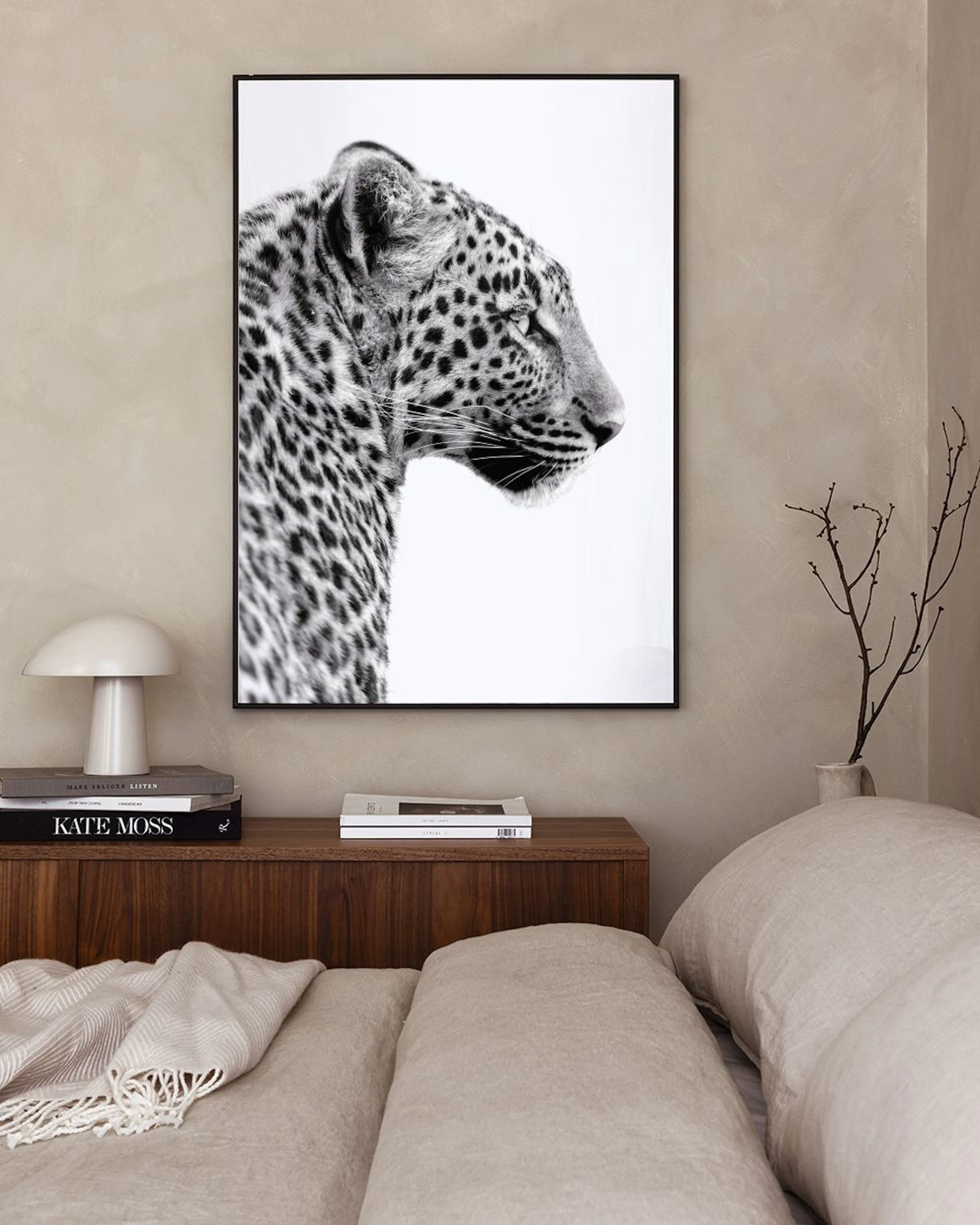 A black and white print of a leopards profile, hanging above a concrete bench with a book, wooden sphere, and glass vase.