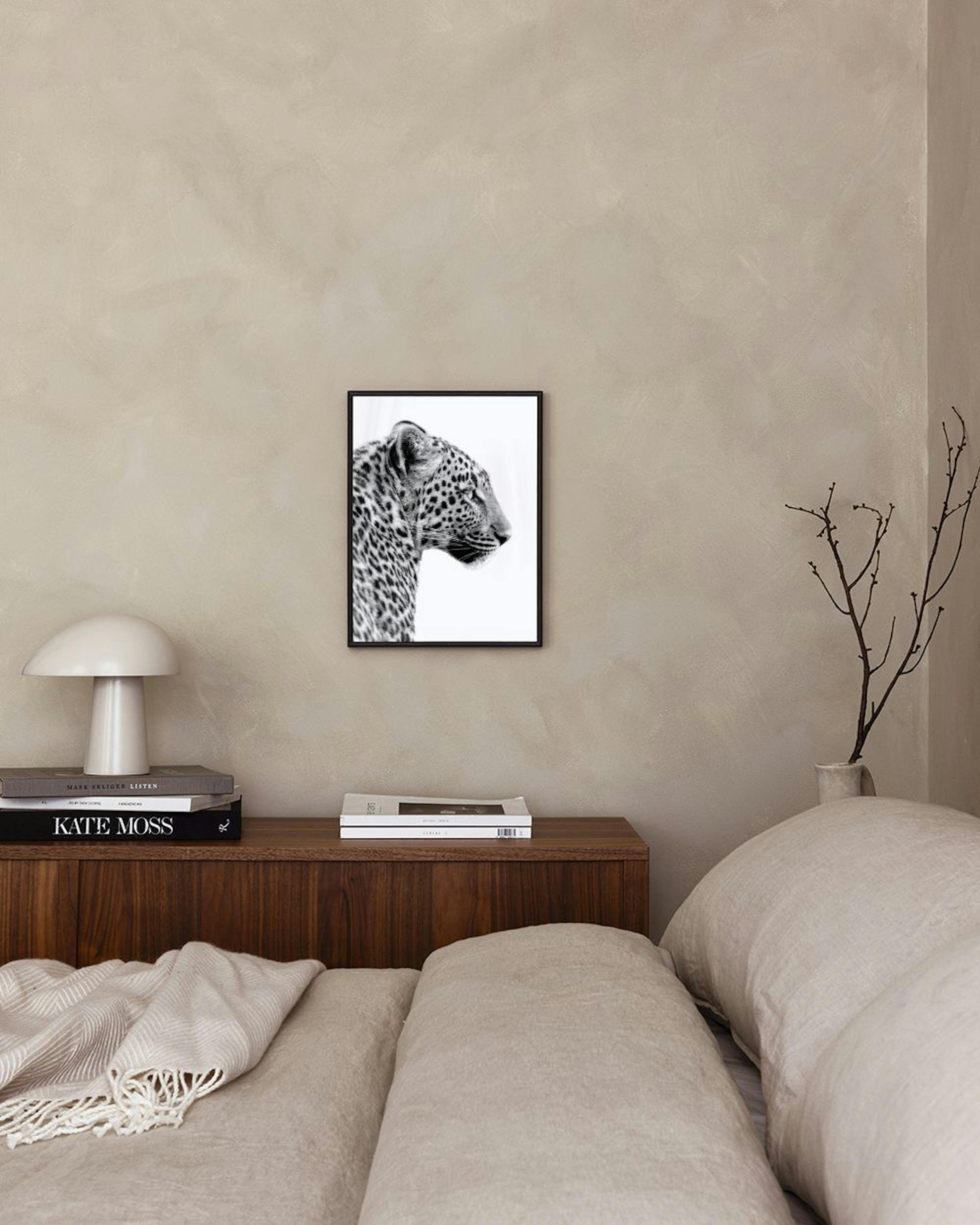 Black and white print of a leopards head in profile, hanging above a concrete bench with a book and glass vase.
