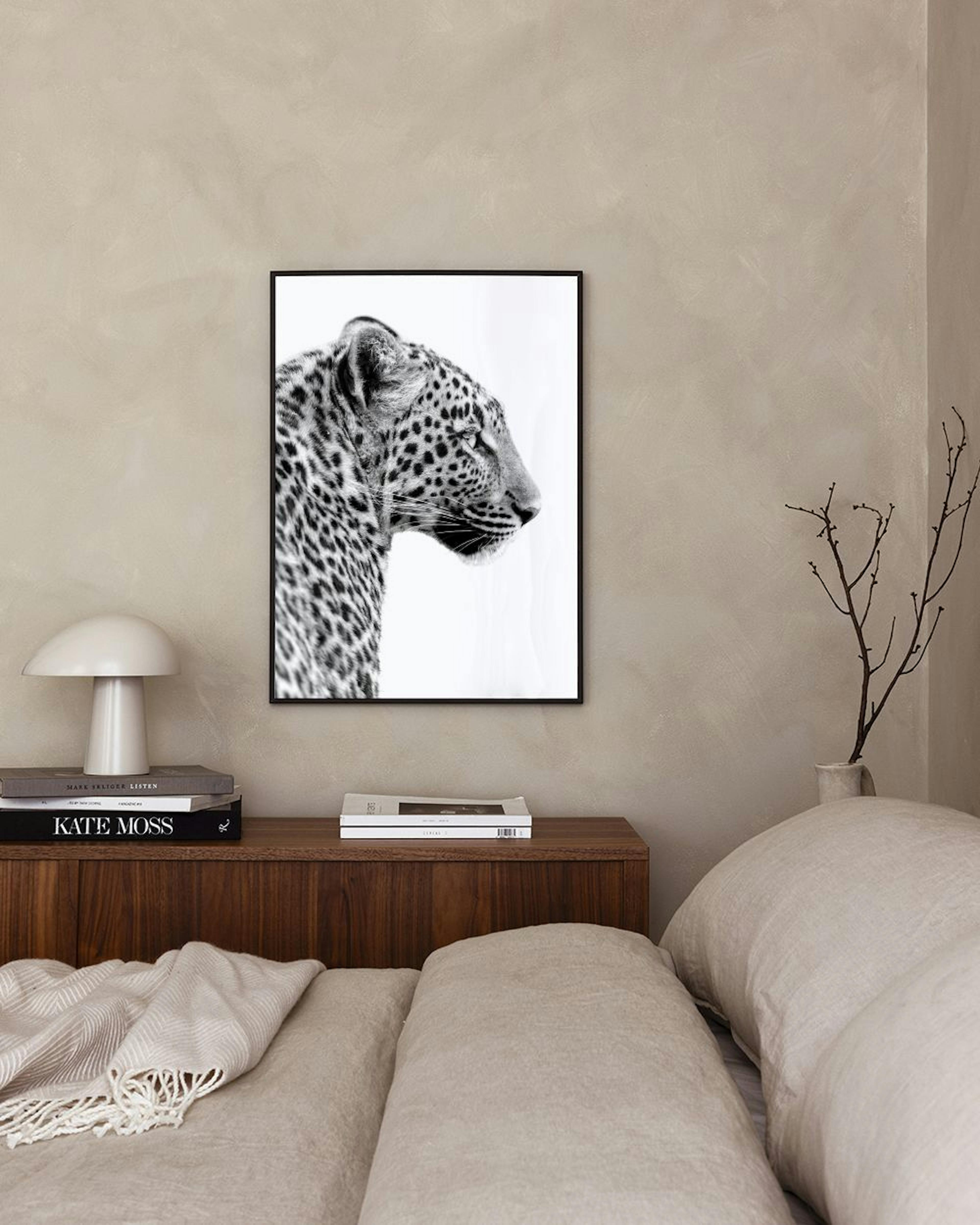 Póster a preto e branco de um leopardo de perfil, pendurado numa parede branca acima de um banco de cimento com um livro aberto 