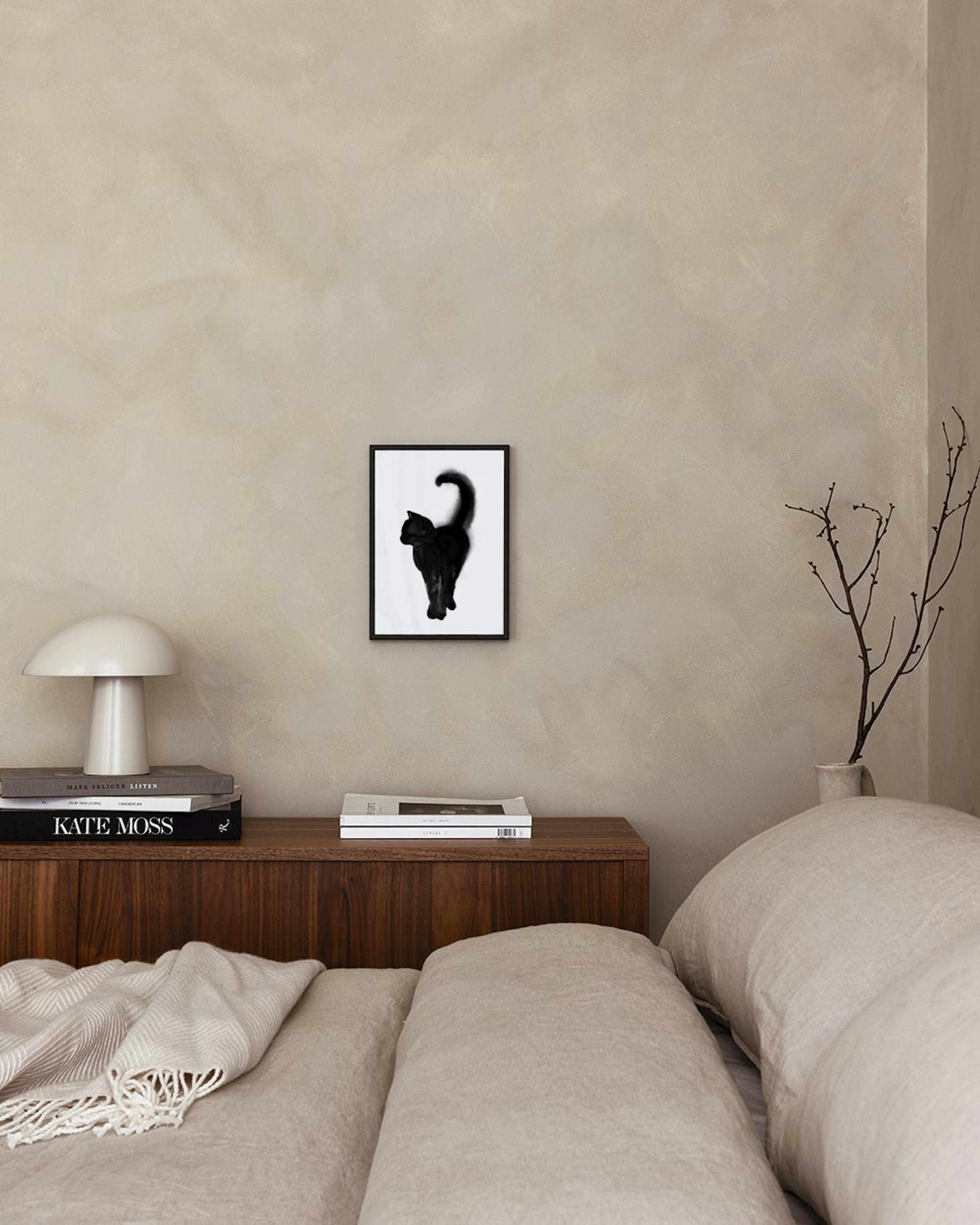 Poster mit schwarzer Katze auf Weiß, über einem Holztisch mit Büchern in einem minimalistischen Raum.