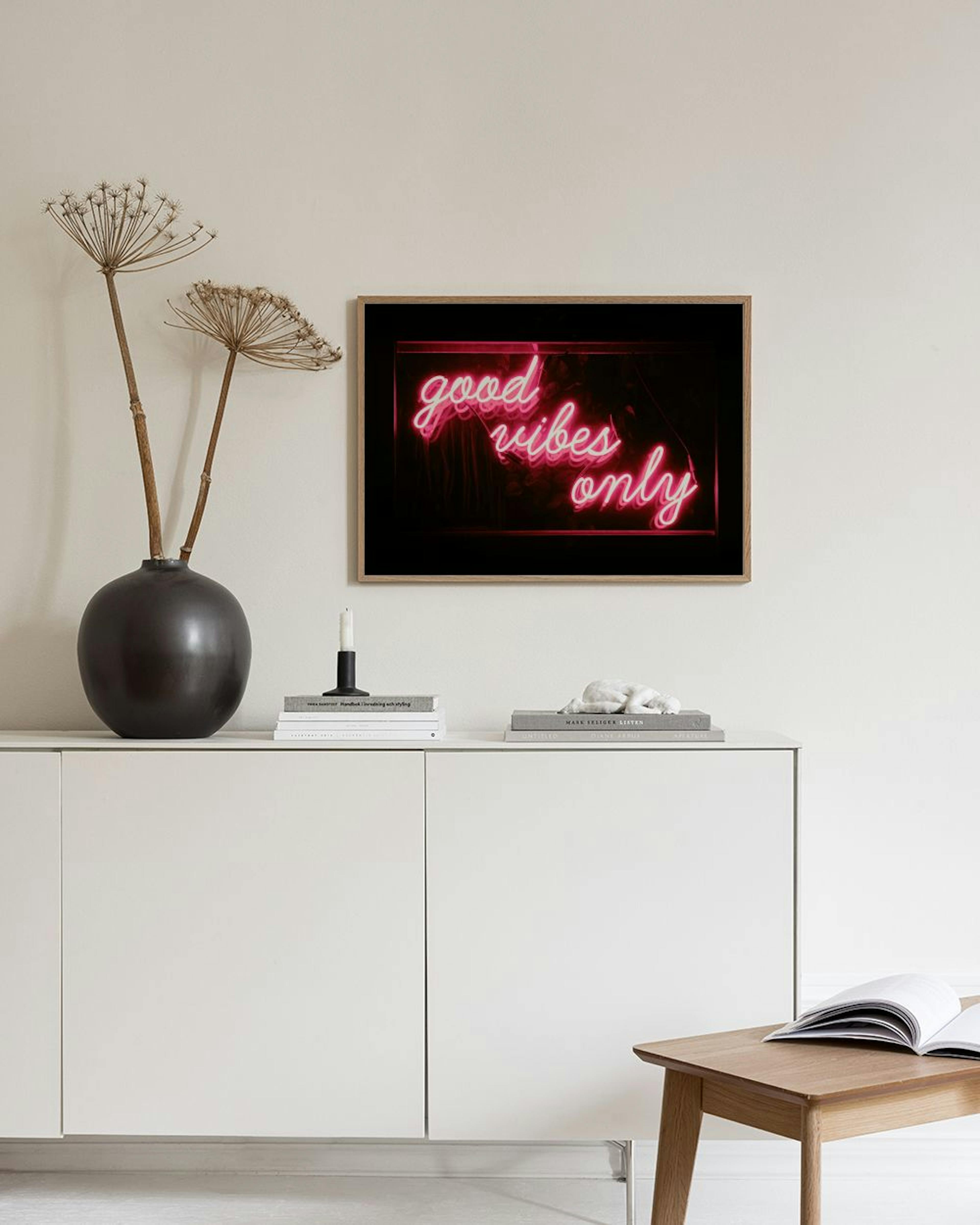 Poster mit leuchtendem Neon-Schriftzug good vibes only in Pink, über einem schwarzen Regal mit Büchern und Deko.