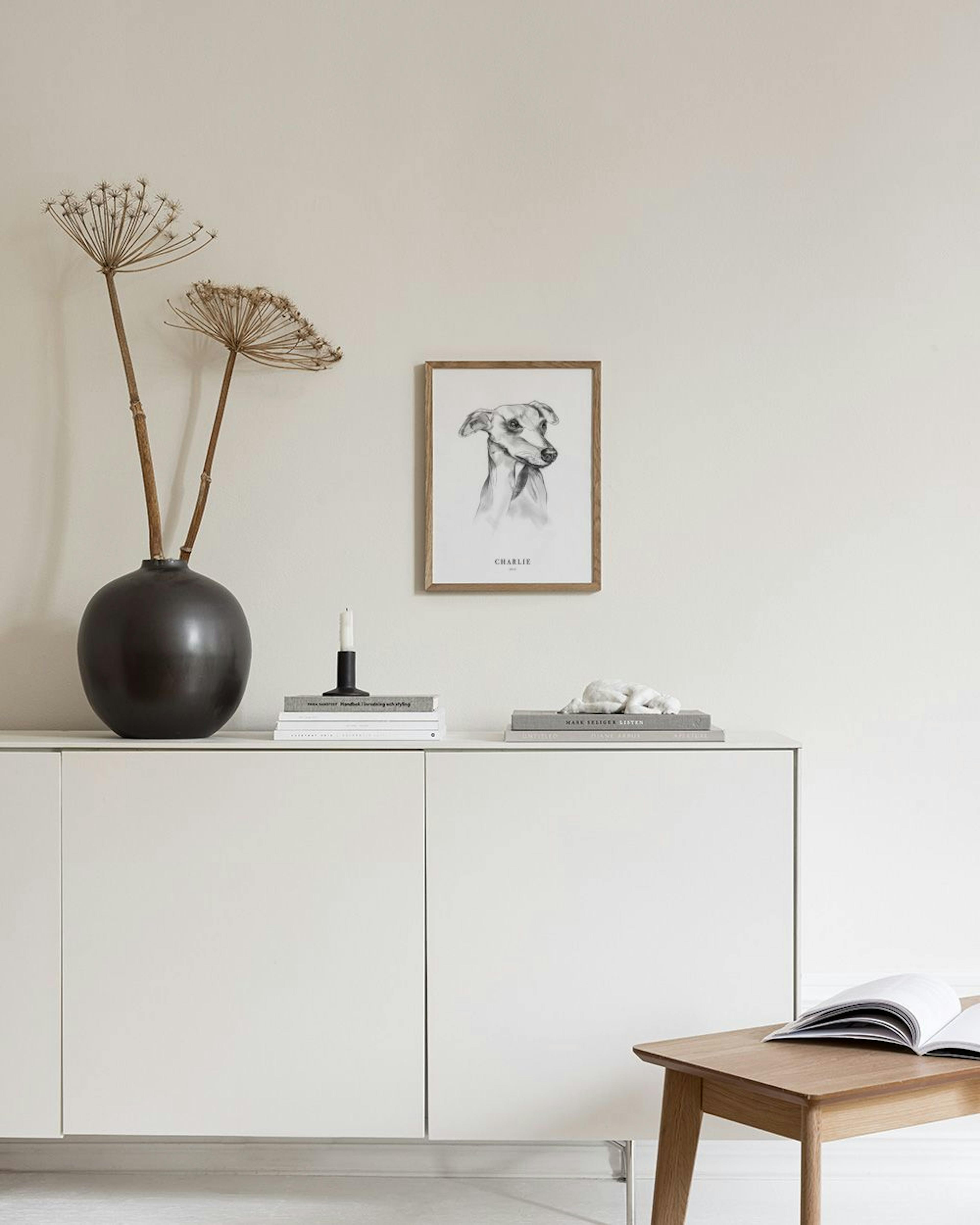 A personalised print of a hand-drawn whippet portrait, named Charlie, hanging above a rustic wooden console table.