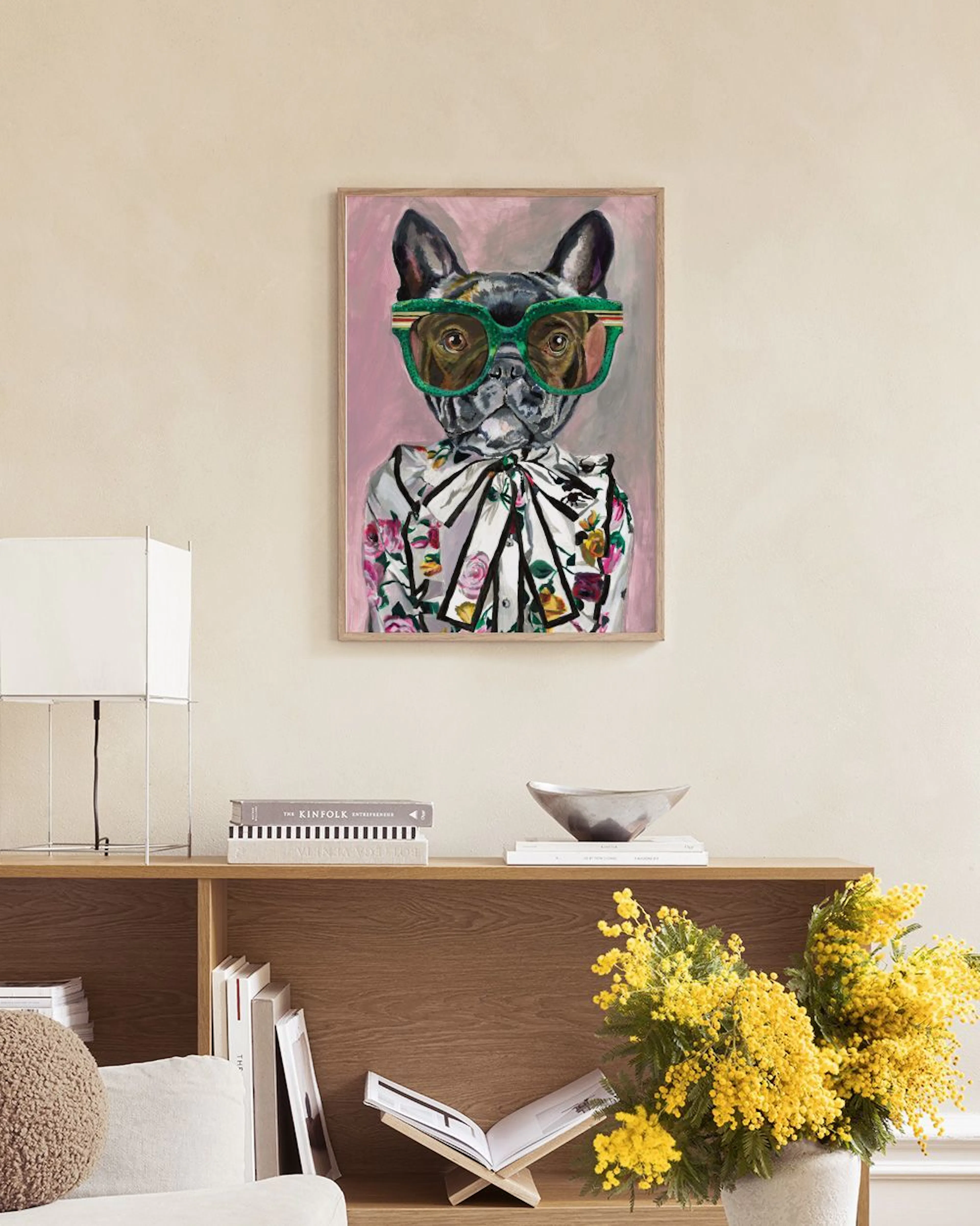 A print of a French Bulldog wearing green sunglasses and a floral shirt, hanging above a pink sofa in a living room.