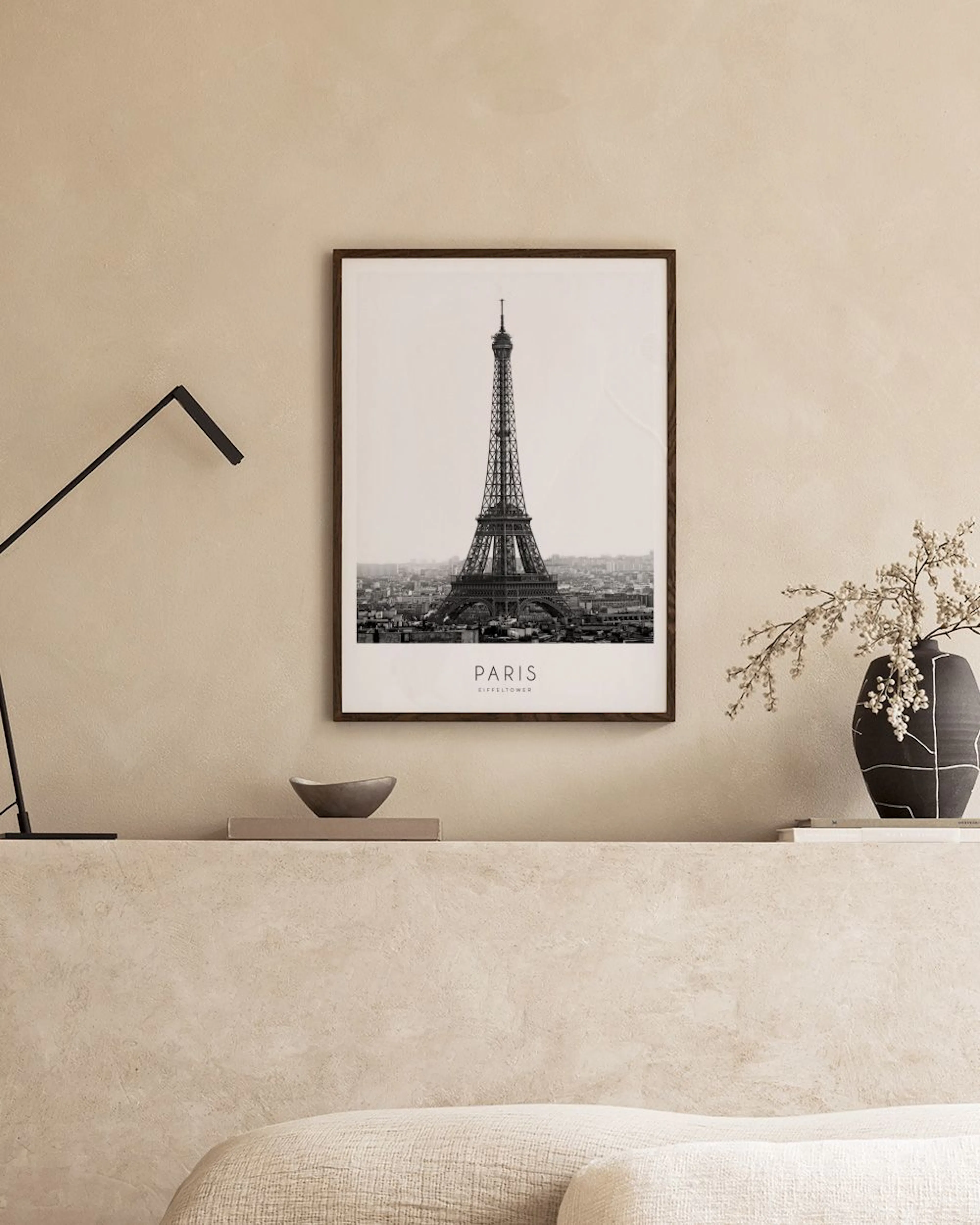 Affiche noire et blanche de la Tour Eiffel à Paris, posée sur une étagère blanche avec des bougies et une plante Monstera.