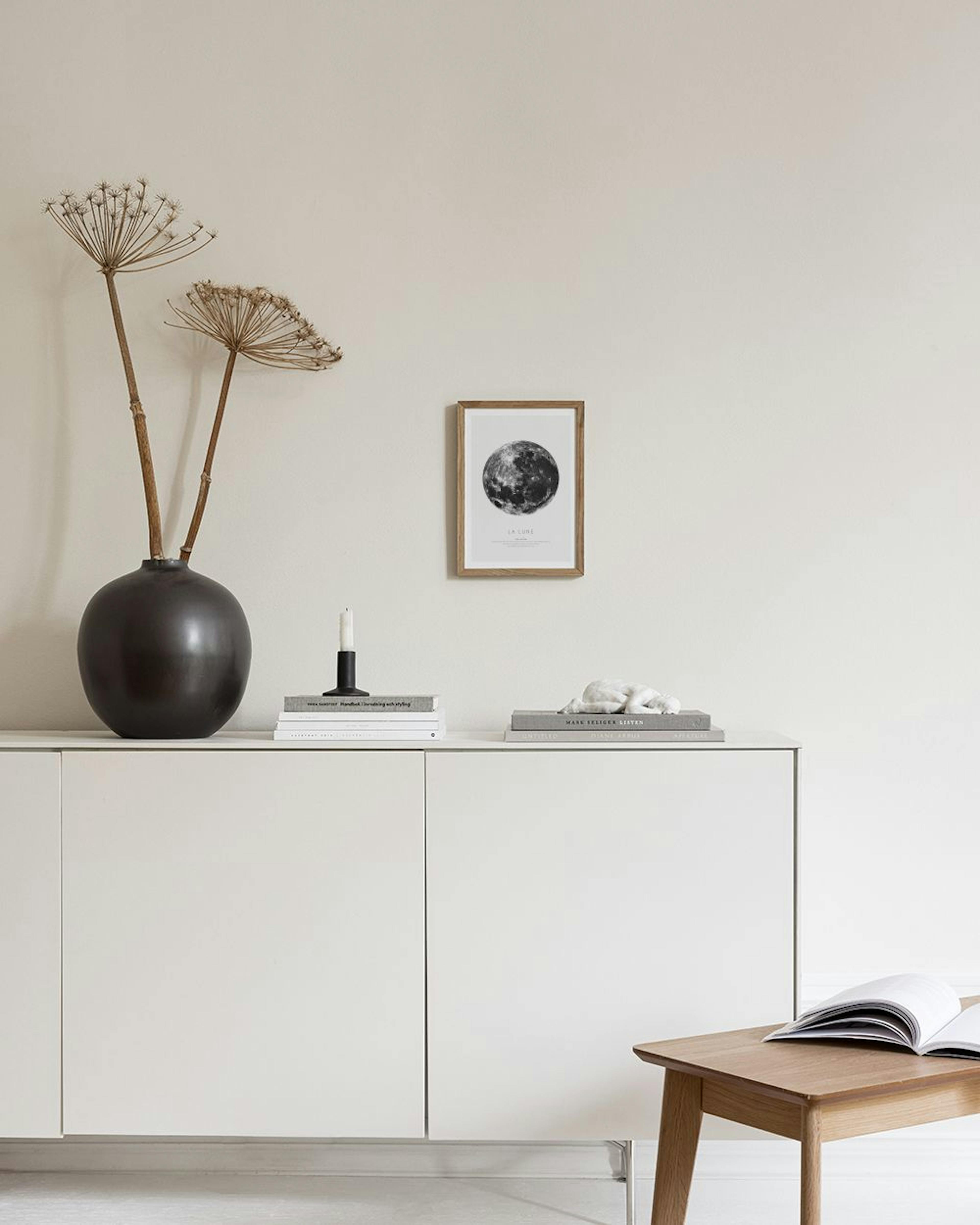 A black and white print of the Moon with text LA LUNE hanging on a blue-gray wall above a white chair with a gray pillow.