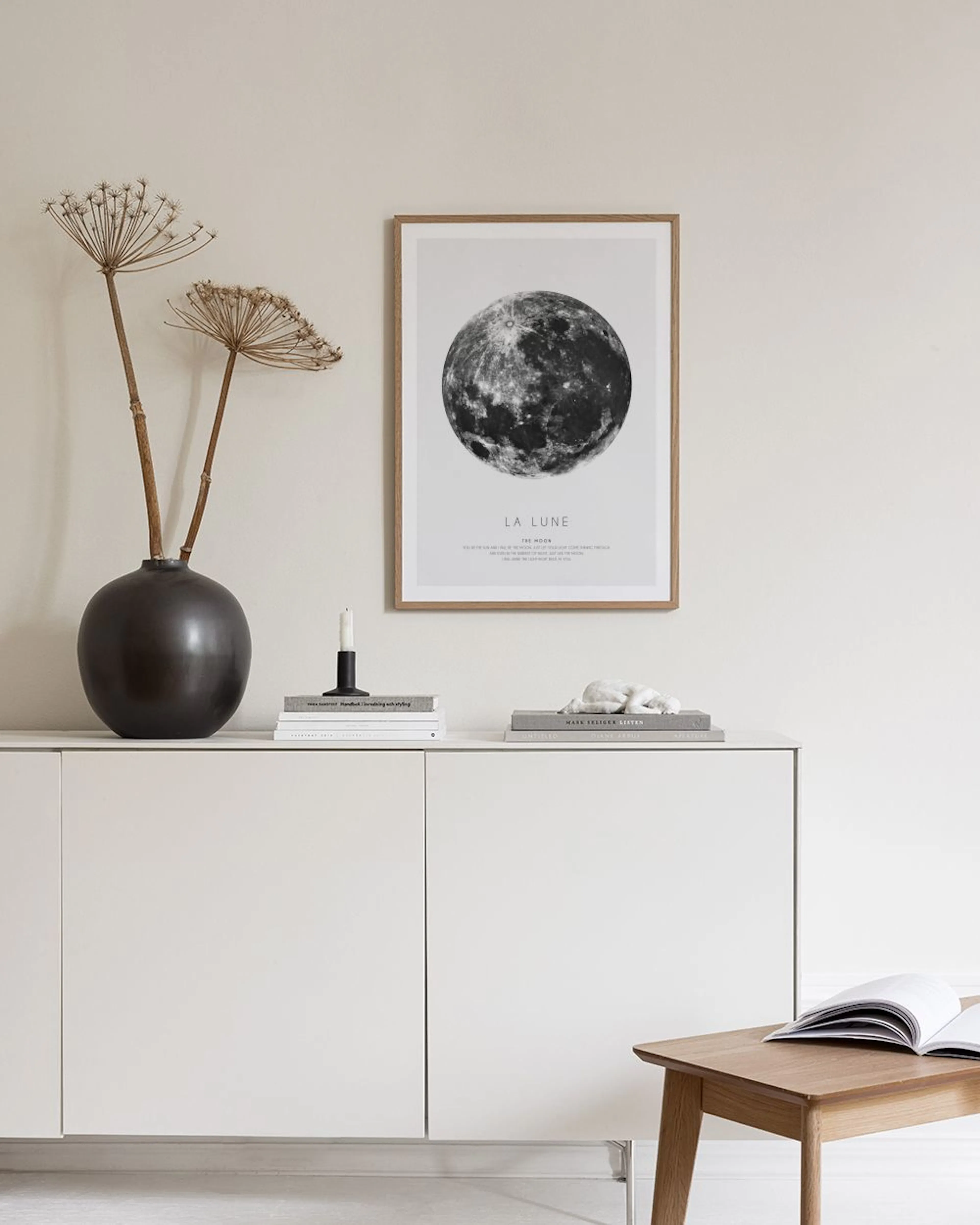 Affiche noire et blanche de la lune, suspendue au-dessus dune chaise blanche avec un coussin gris dans un décor moderne.