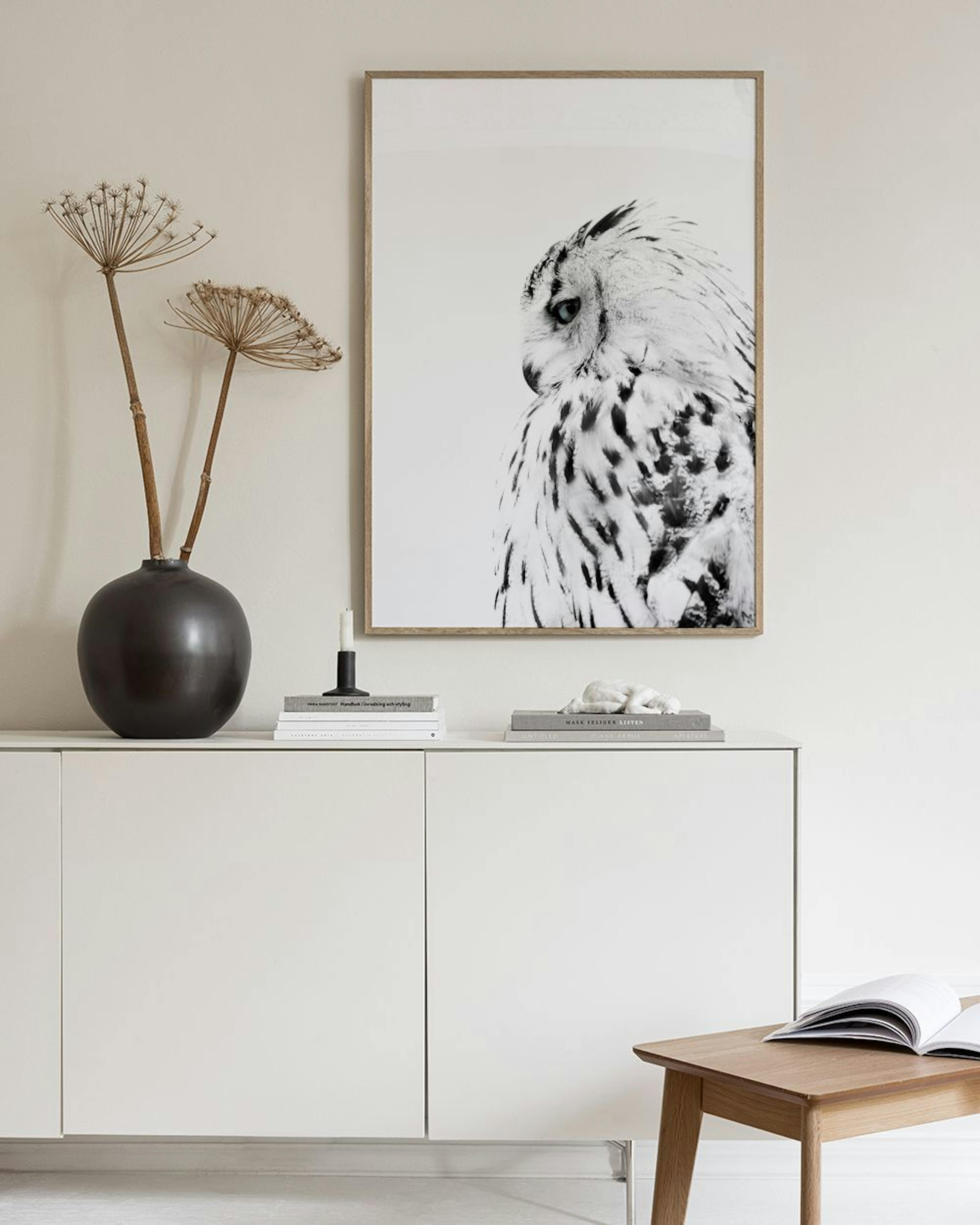 Monochrome print of a snowy owl on a light gray wall, with two glass bottles and a black chair nearby.