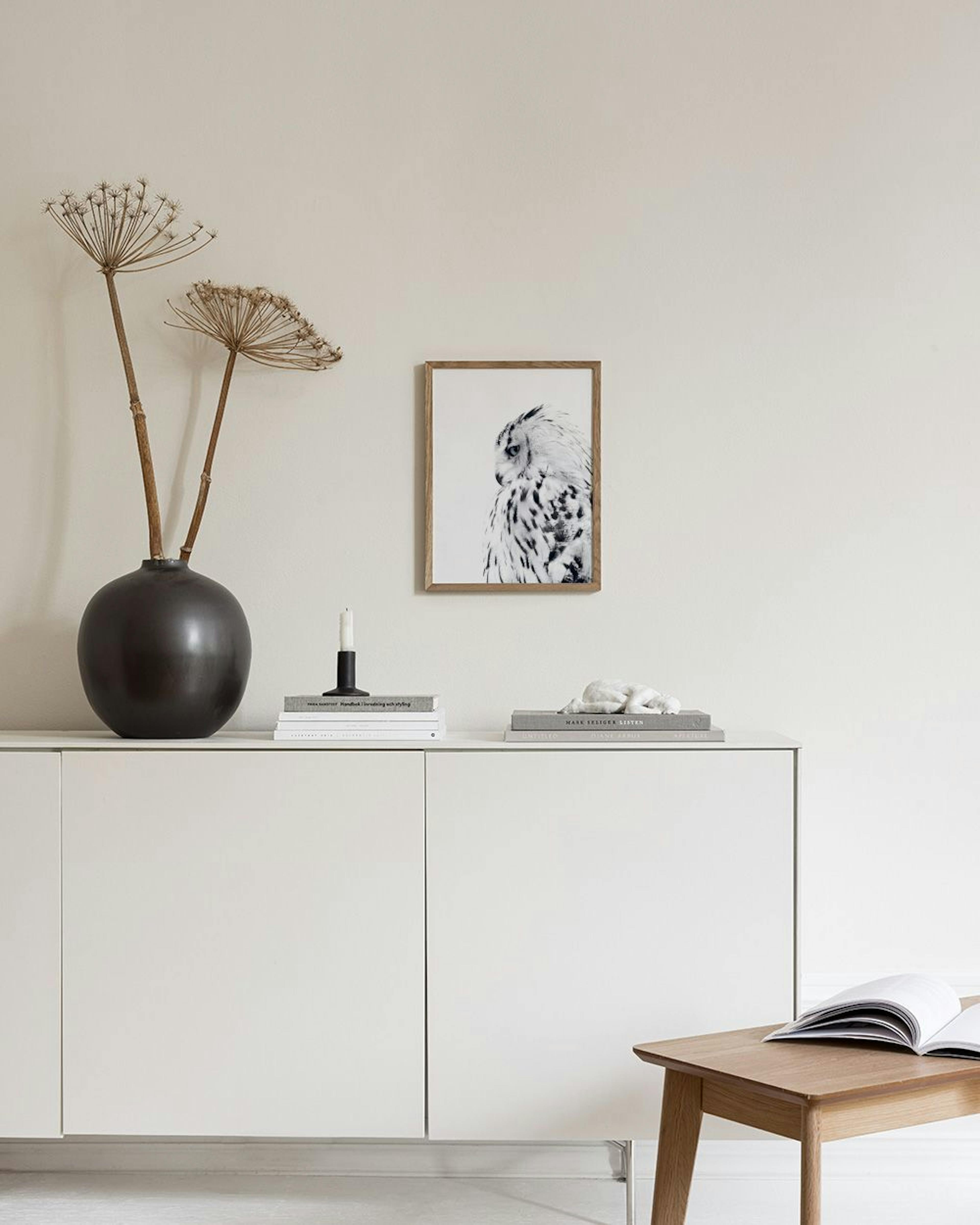 Affiche dun hibou des neiges en noir et blanc, accrochée au mur dans un salon moderne avec une chaise et des vases.