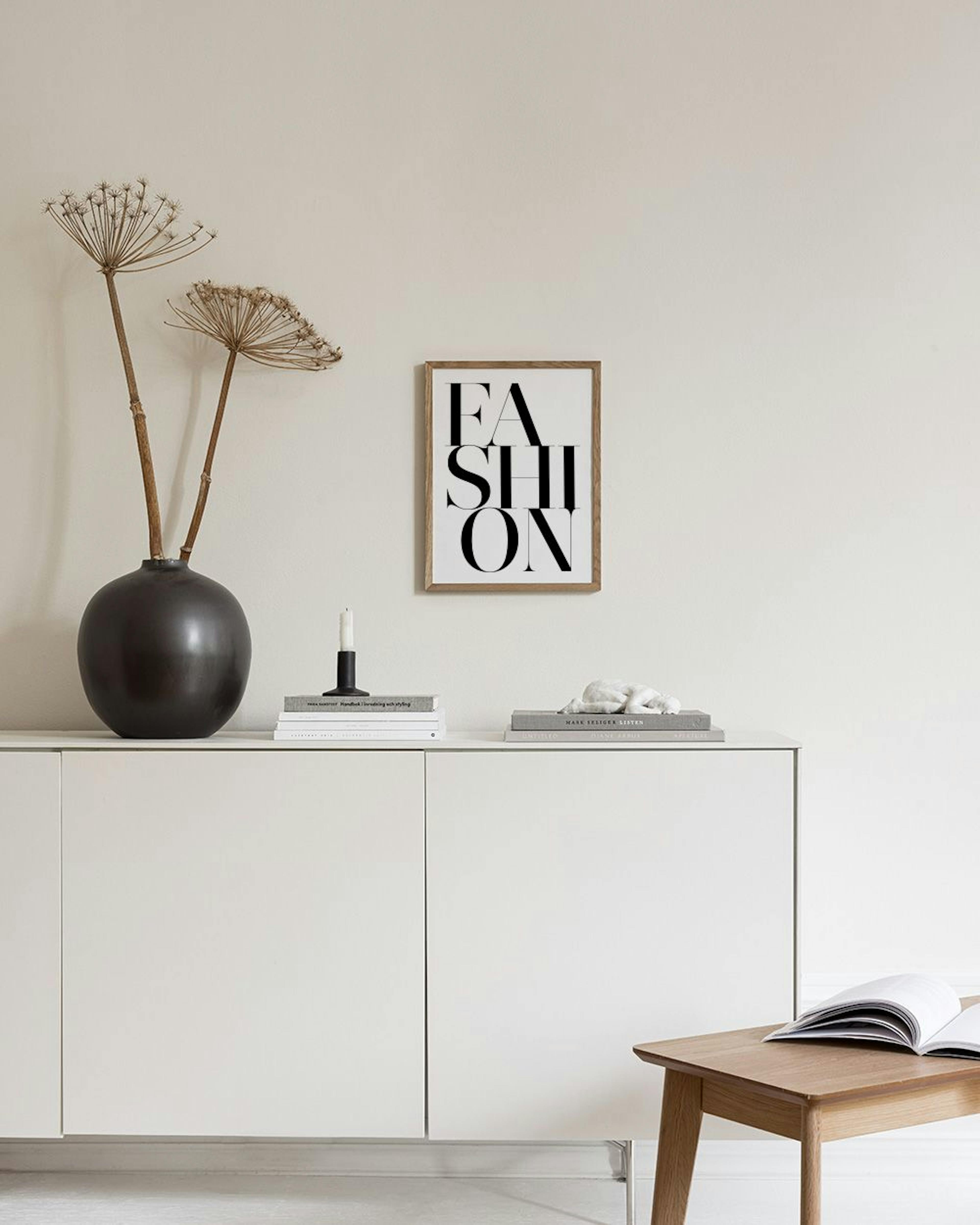 Πόστερ με τη λέξη FASHION σε μαύρα γράμματα, κρεμασμένο σε μαύρο δικτυωτό πίνακα, με ένα μαύρο τραπέζι και βάζα.