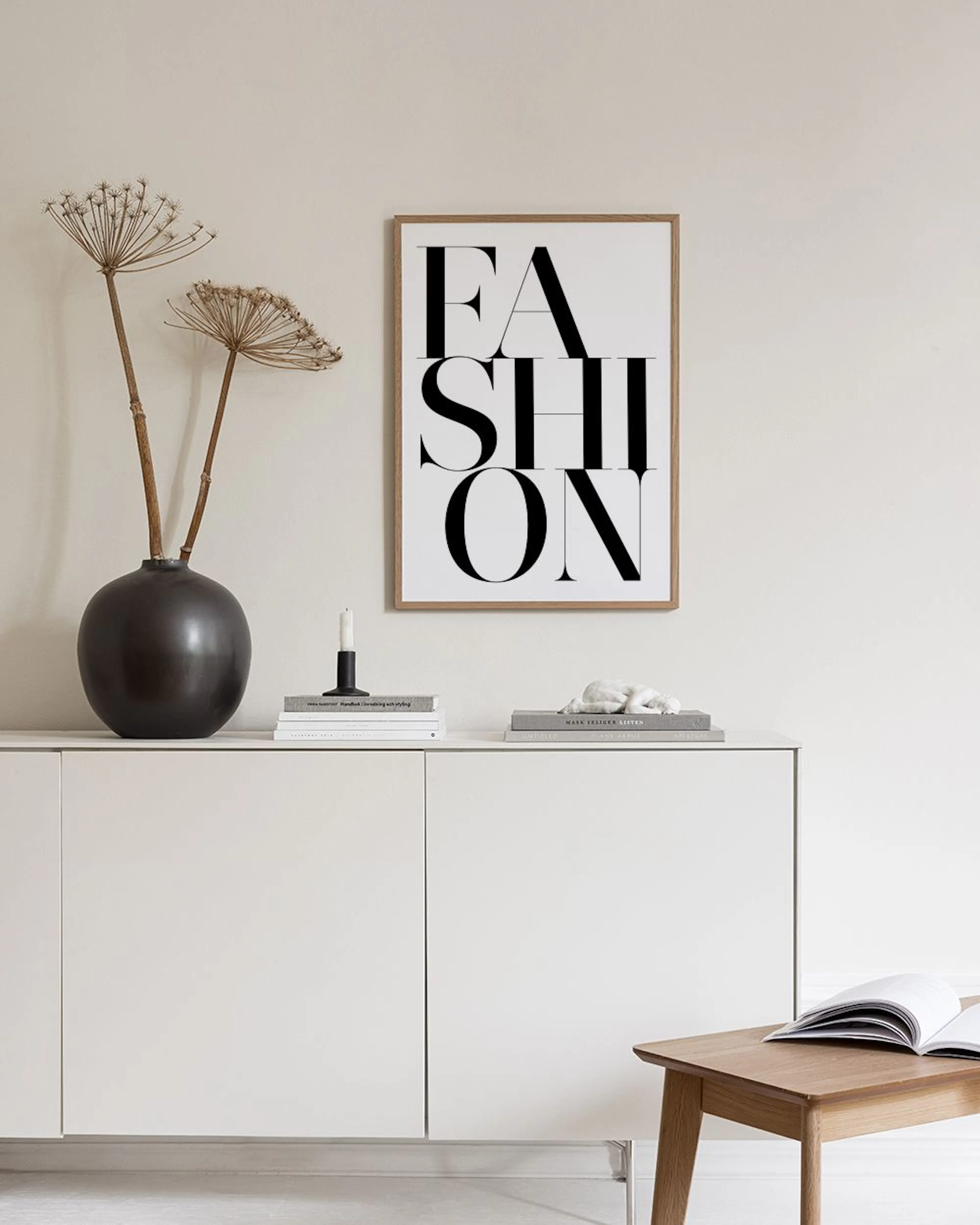 Ein Poster mit dem Wort FASHION“ in Schwarz auf weißem Grund, hängt an einer Gitterwand in einem modernen Raum.