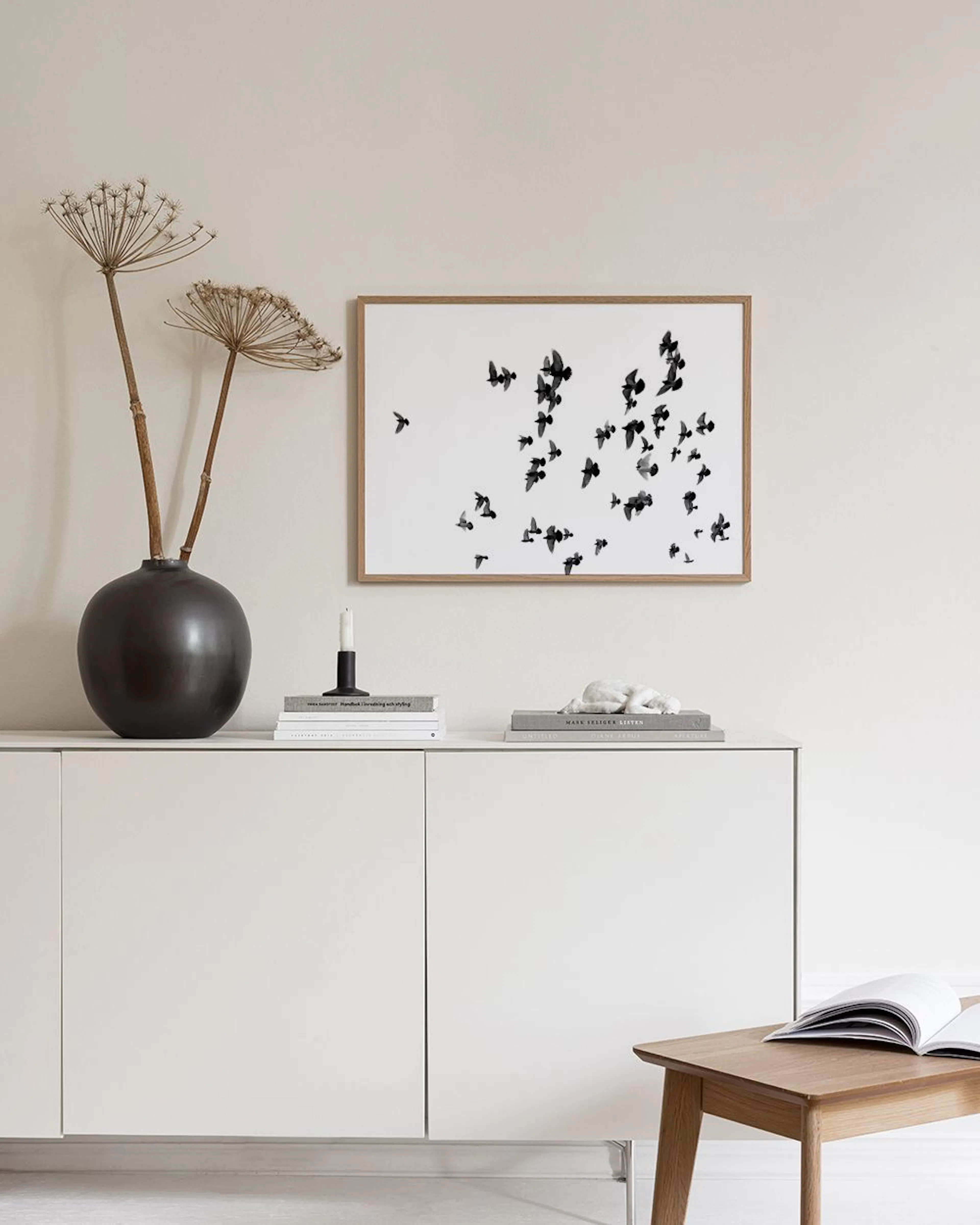Affiche avec des silhouettes doiseaux noirs en vol sur fond blanc, accrochée dans une pièce minimaliste.