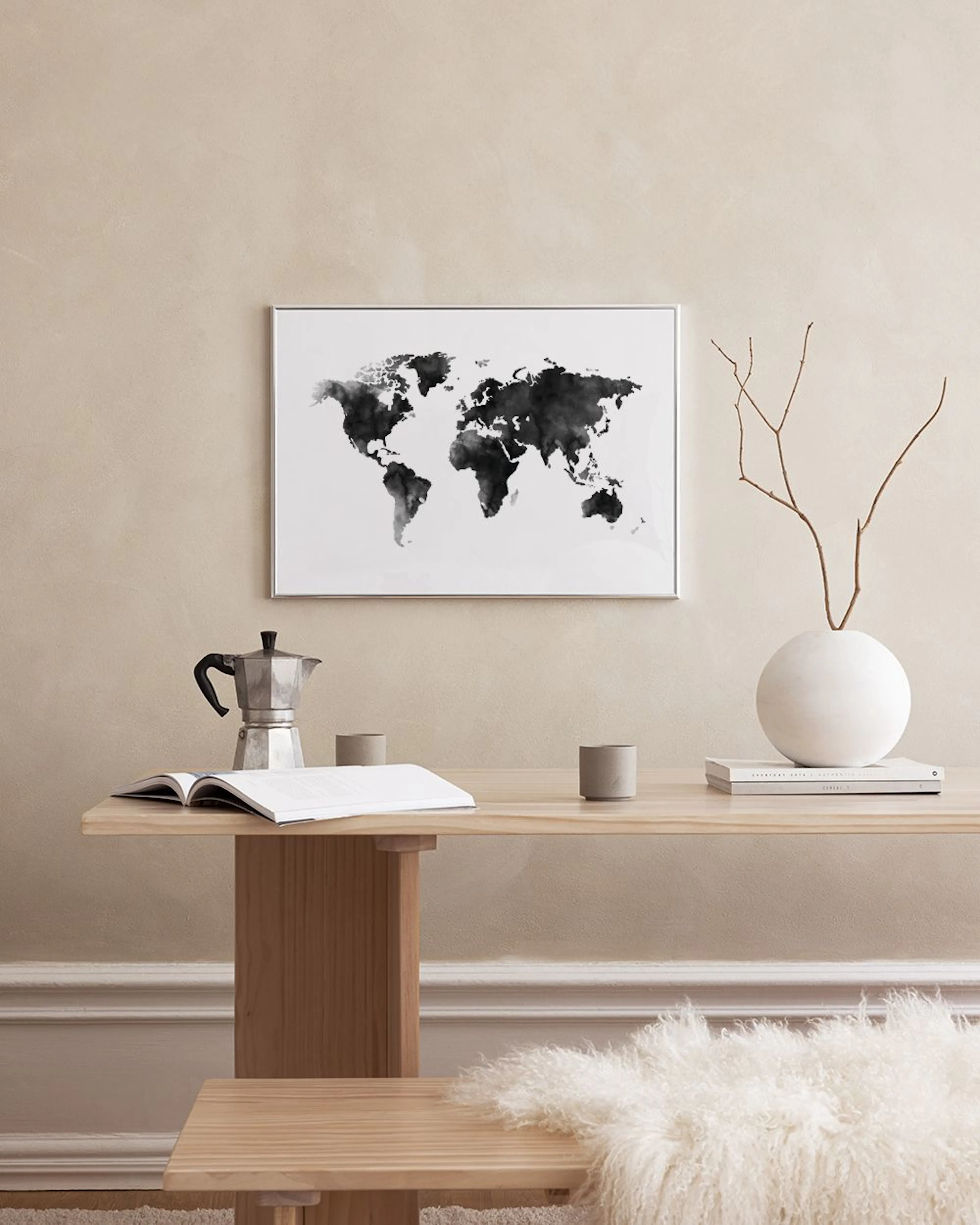 A black and white watercolour map print hanging on a dark teal wall above a black metal table with books and glass bottles.