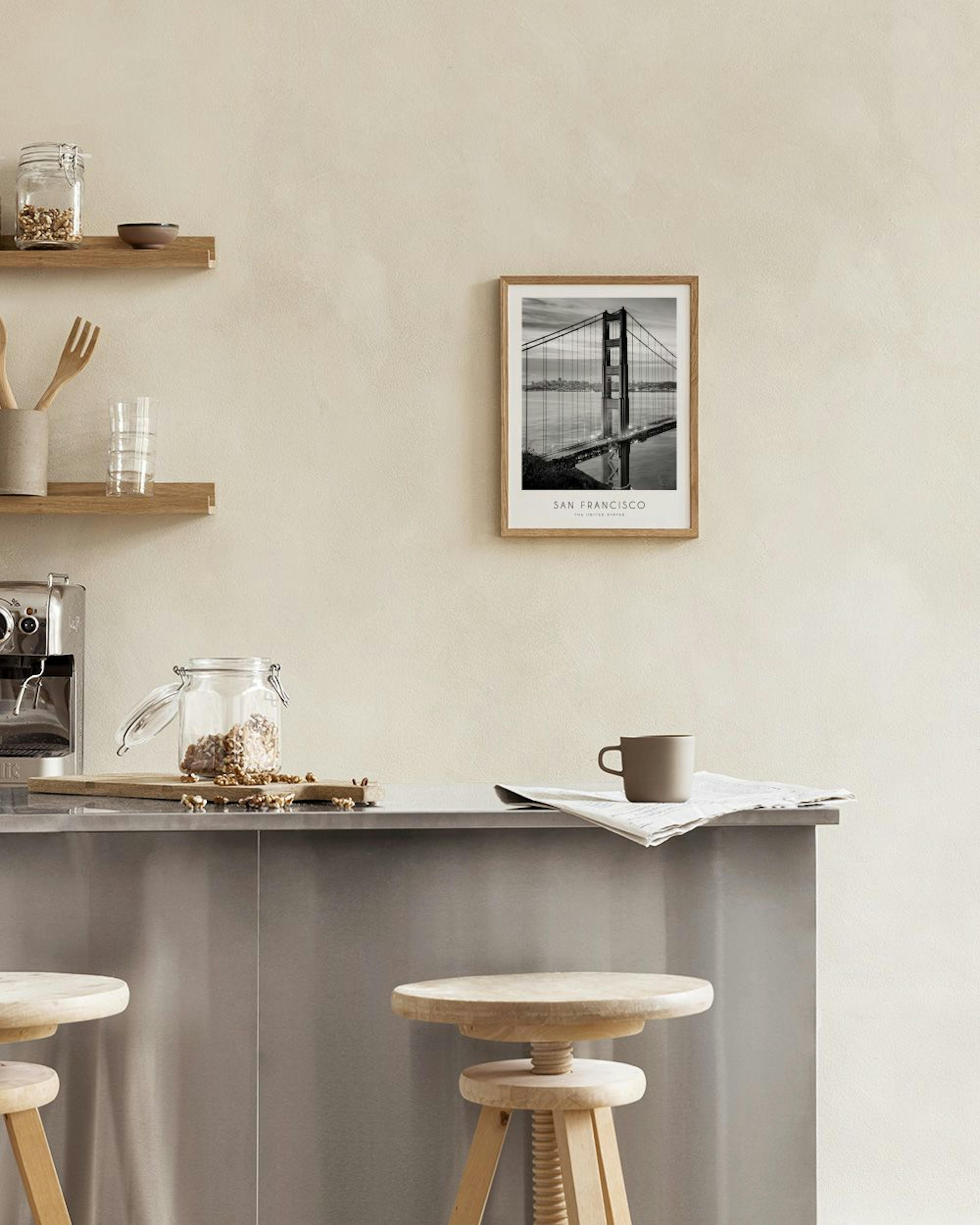A black and white print of the Golden Gate Bridge hangs above books and a candle on a black table.