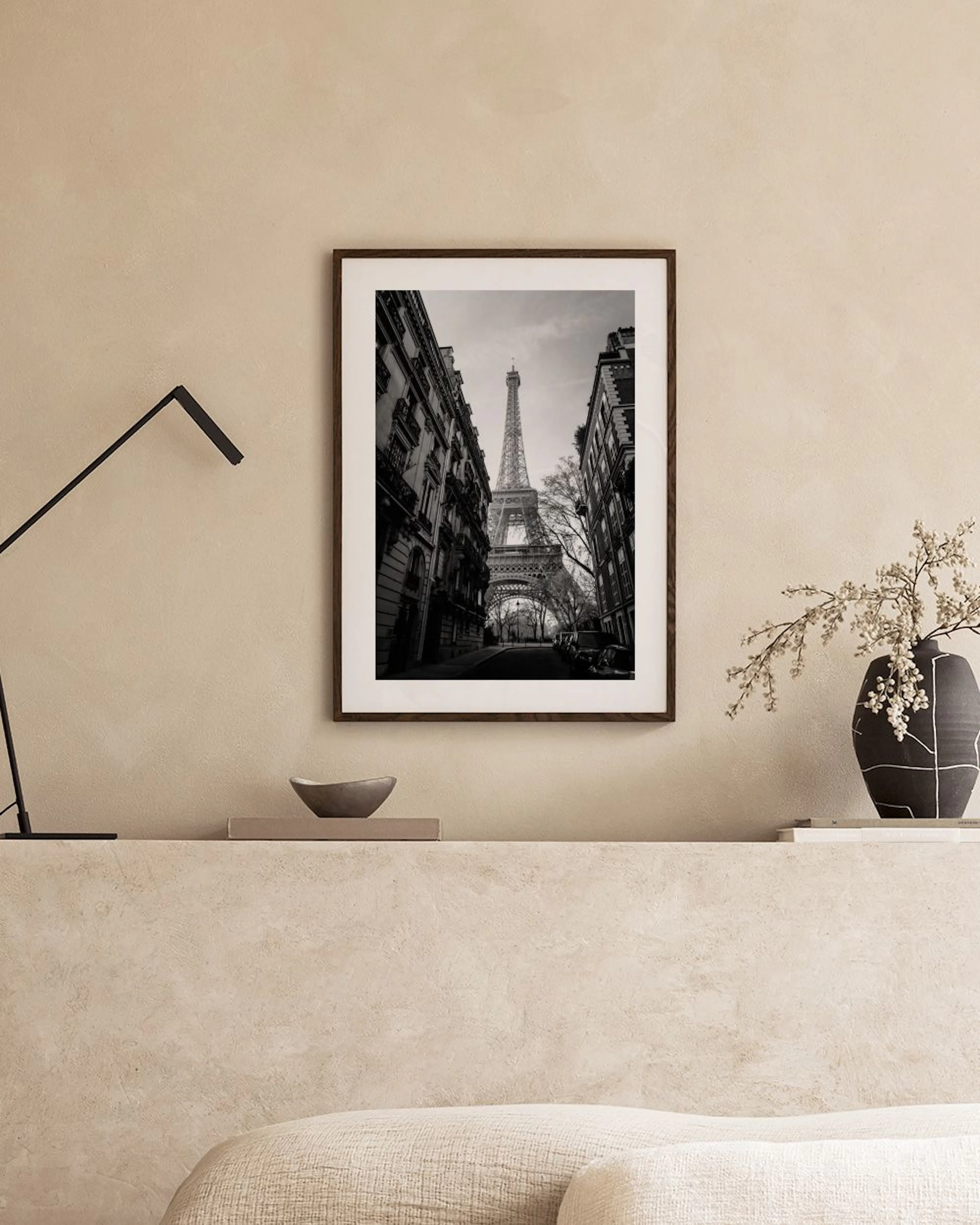 A black and white print of the Eiffel Tower seen from a Parisian street, hanging above a teal velvet stool and a black console t