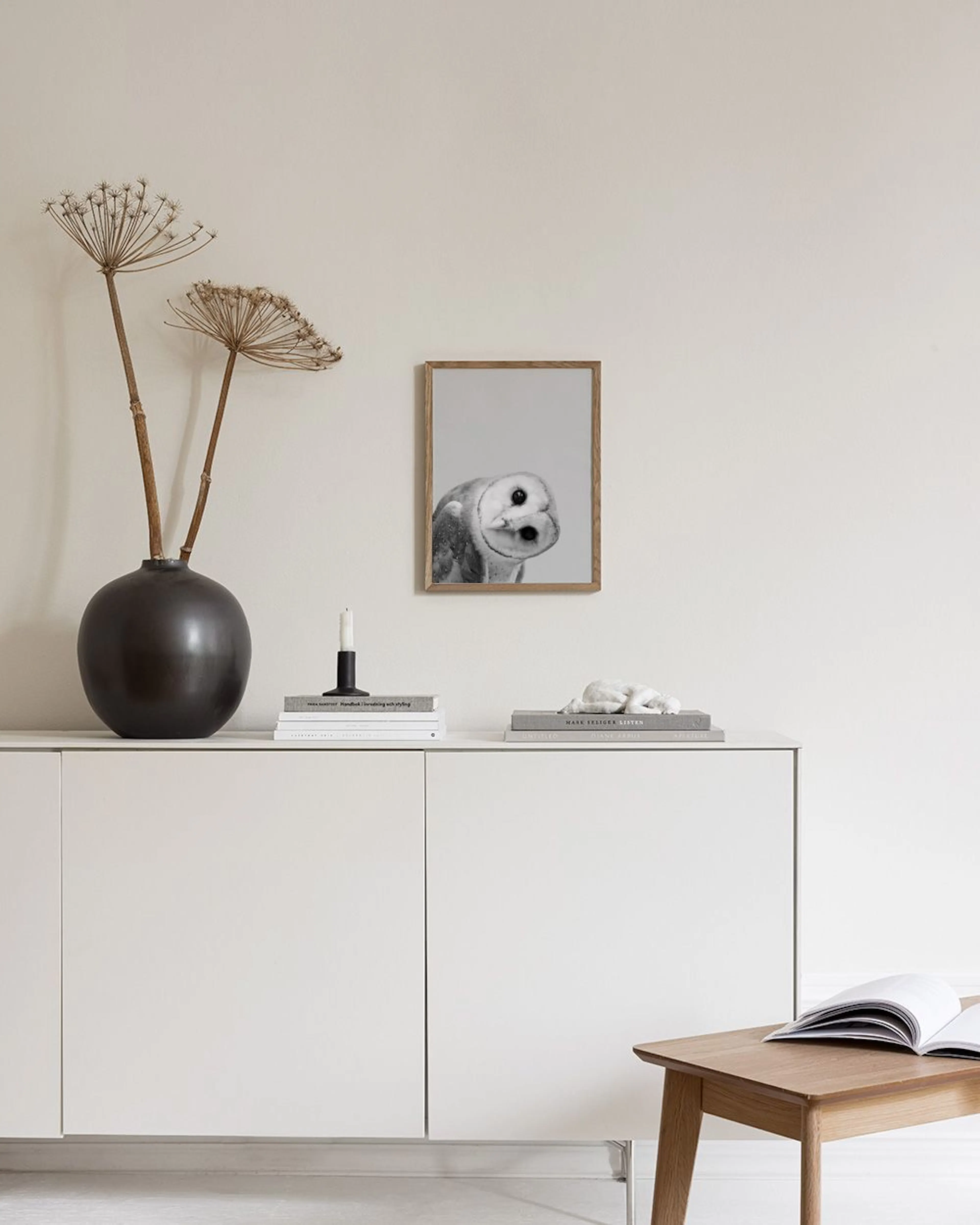 A black and white print of a barn owl with its head tilted, displayed above a white cabinet with decorative items.