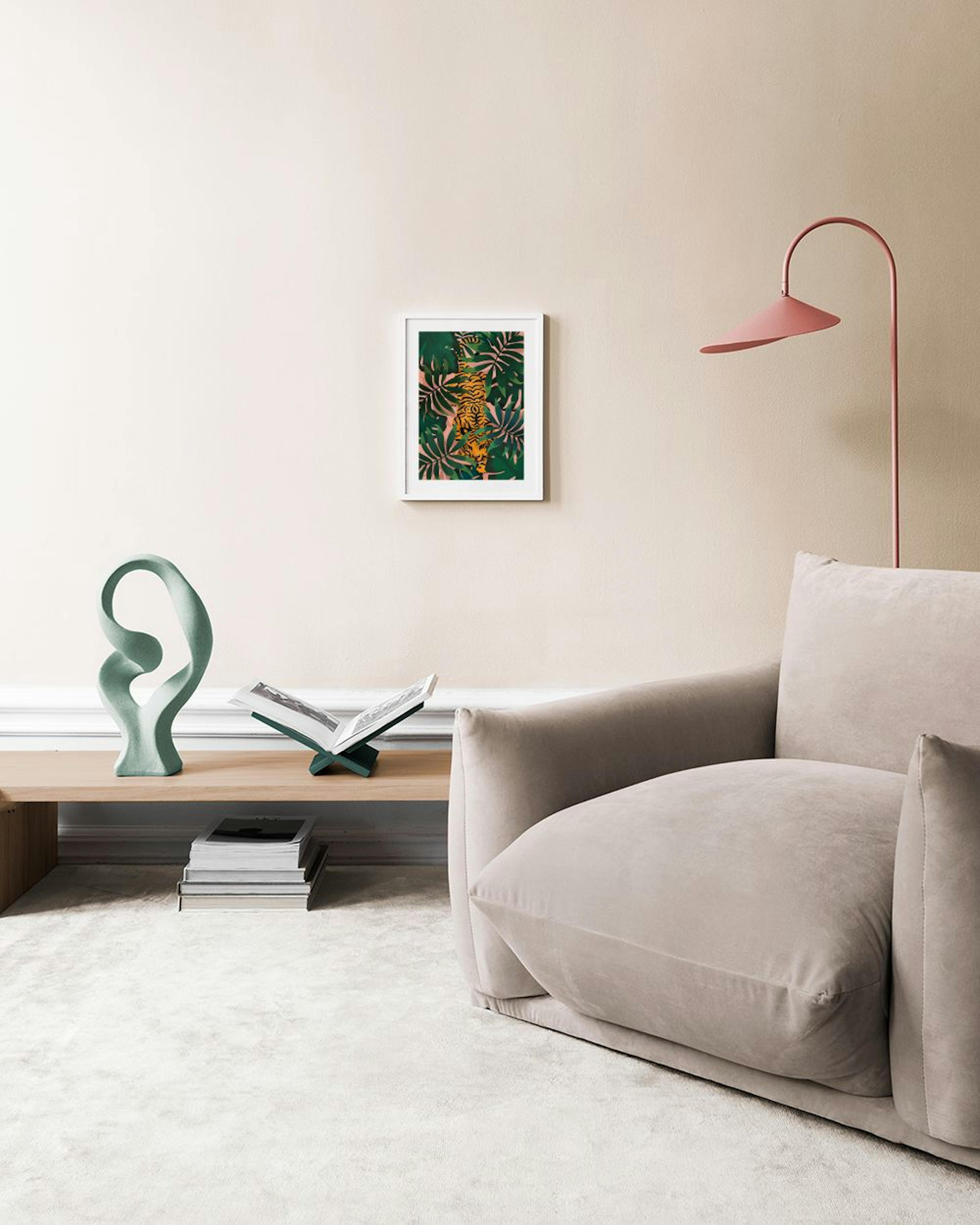 A jungle print with an orange tiger and green leaves, hanging on a gray wall above two potted plants and stacked pillows.