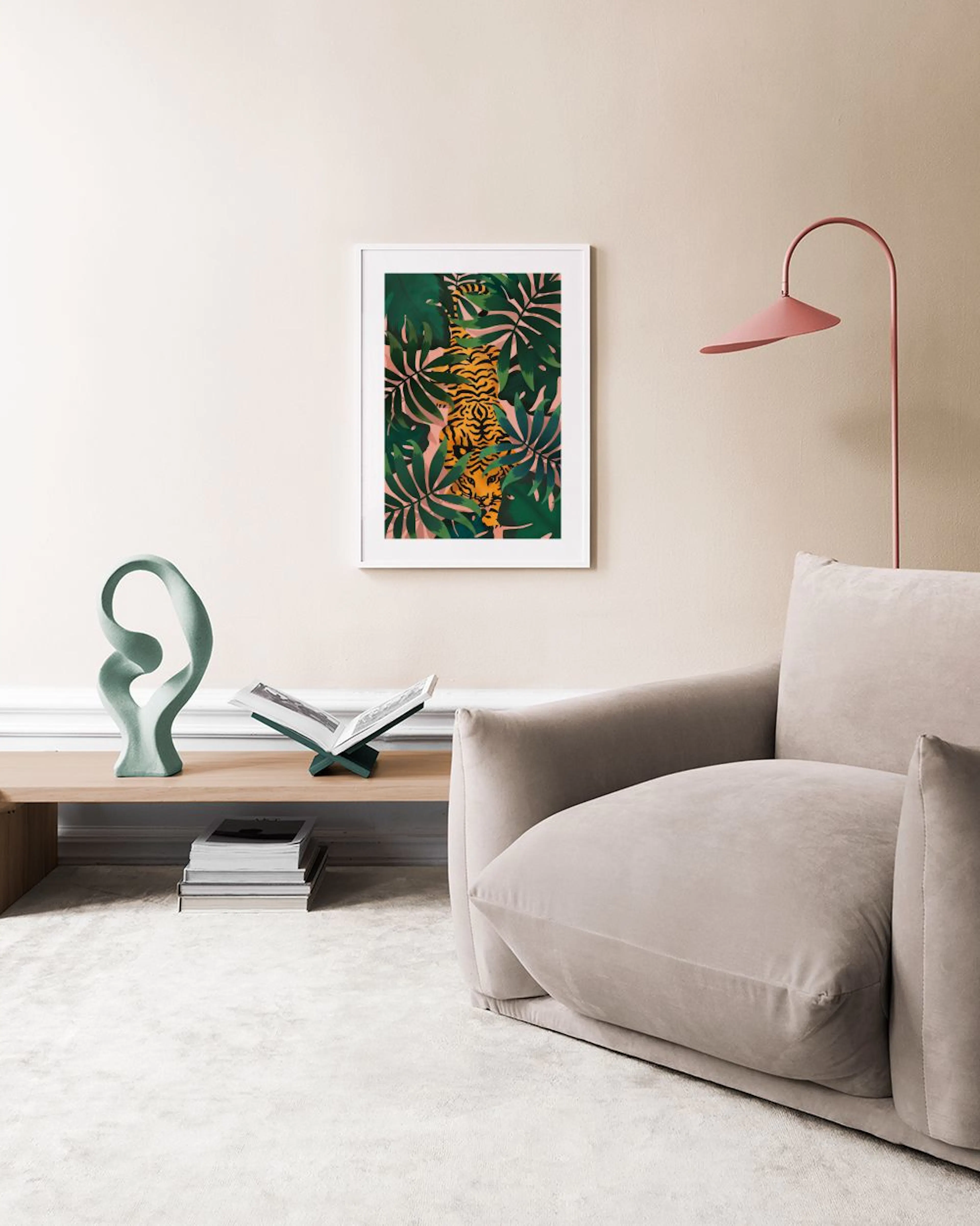 A jungle print with an orange tiger and green leaves, hanging on a gray wall above two potted plants and stacked pillows.