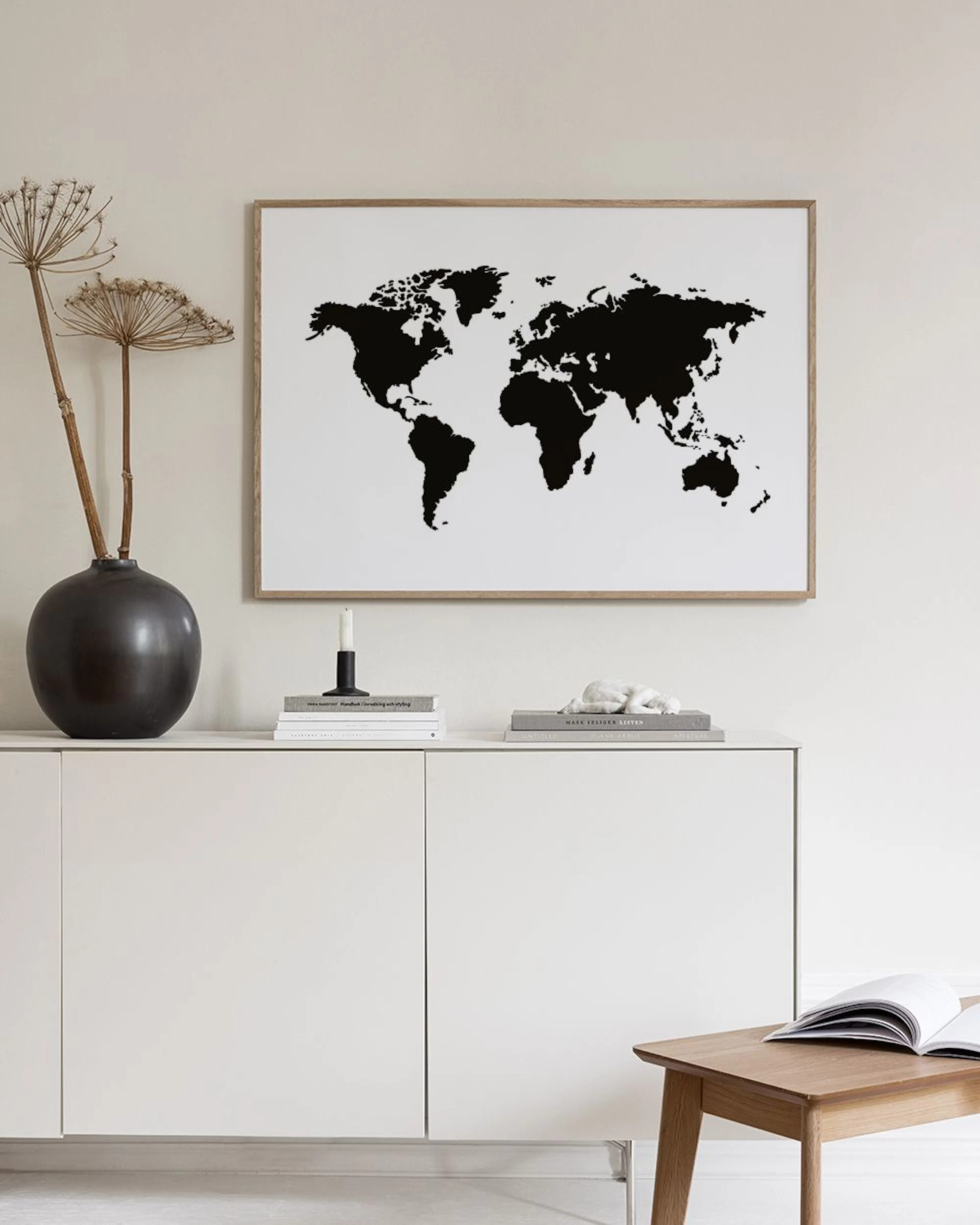 A minimalist world map print with black continents on a white background, hanging on a teal wall above a black metal console tab