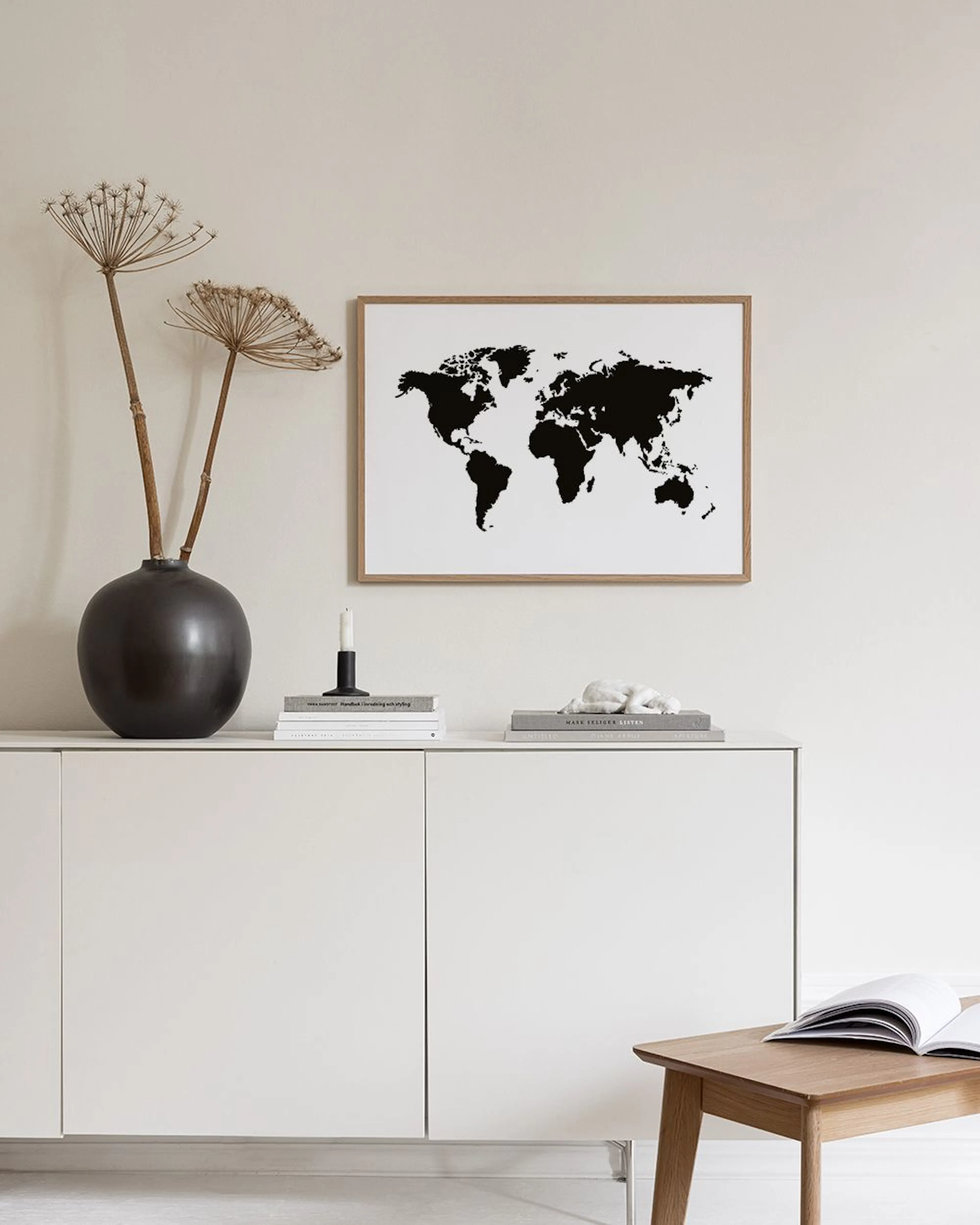 A minimalist black and white world map print hanging on a teal wall above a black metal table with books and decor.