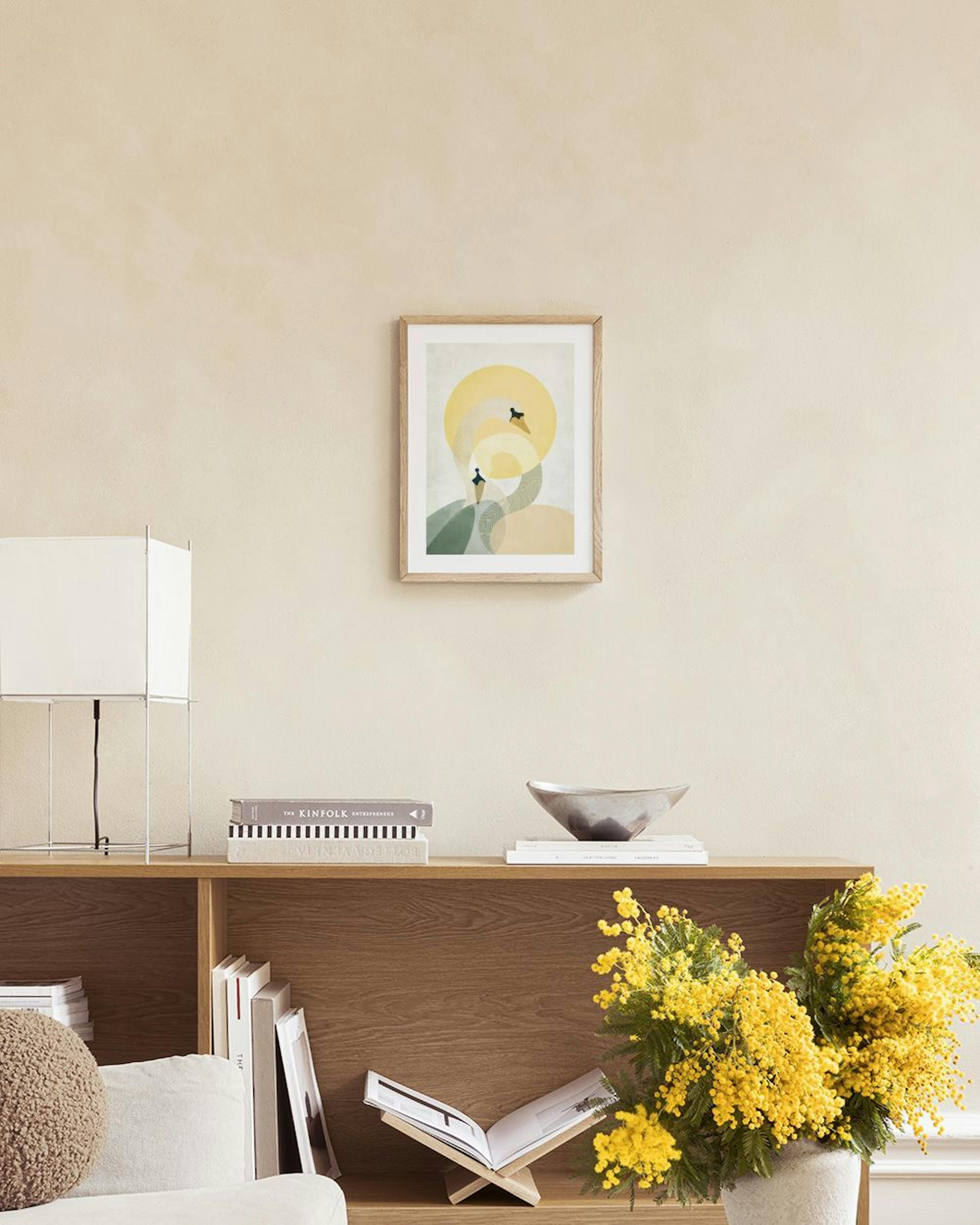 A print of two abstract swans with yellow, green, and beige geometric shapes, hanging above a concrete side table beside a ratta