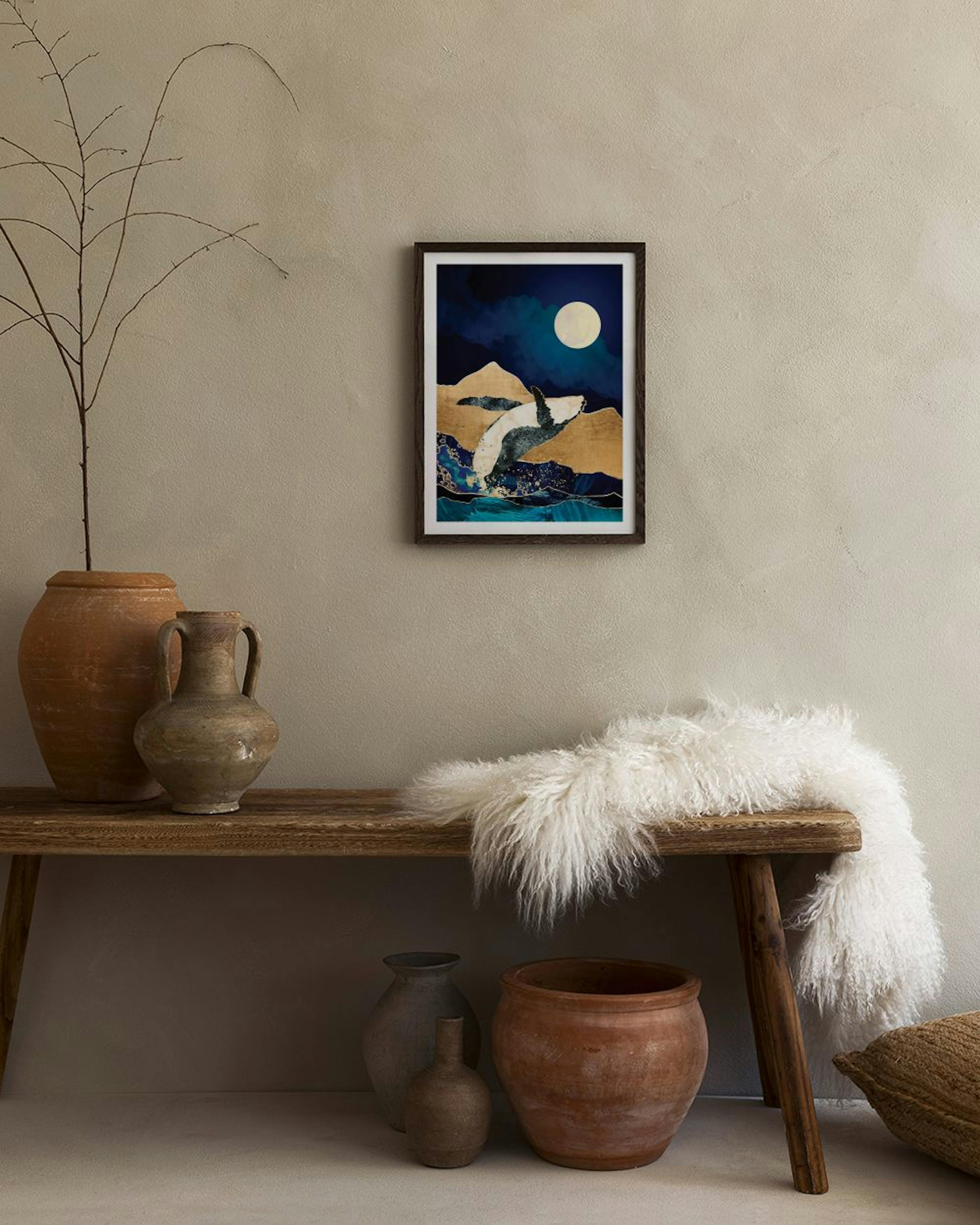 A print of a whale breaching from blue waves into golden mountains under a full moon, displayed above a black console table.