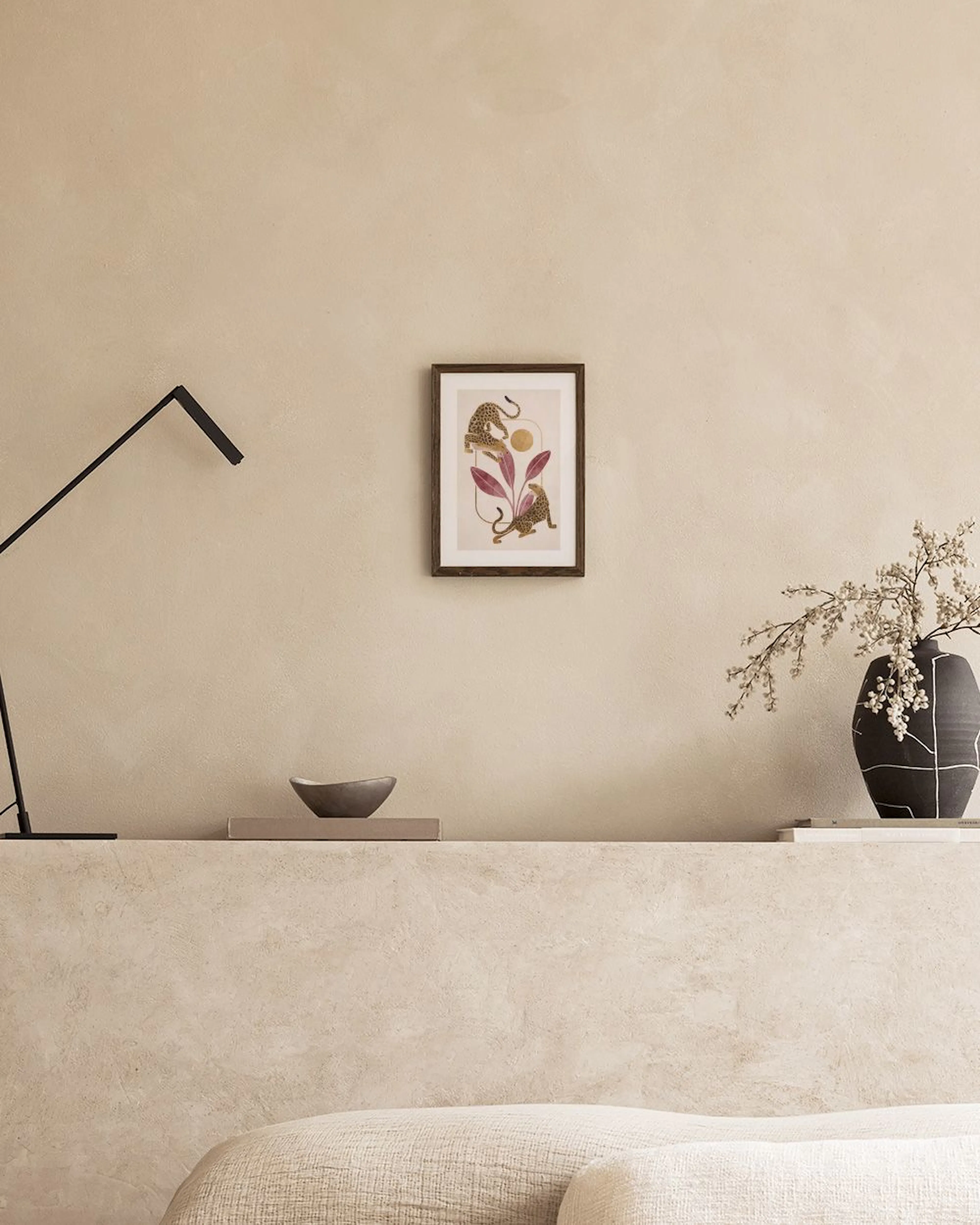 Poster mit zwei Leoparden, die auf roten Blättern klettern, und goldenen Details, über einem weißen Sideboard mit Vase und Buch.