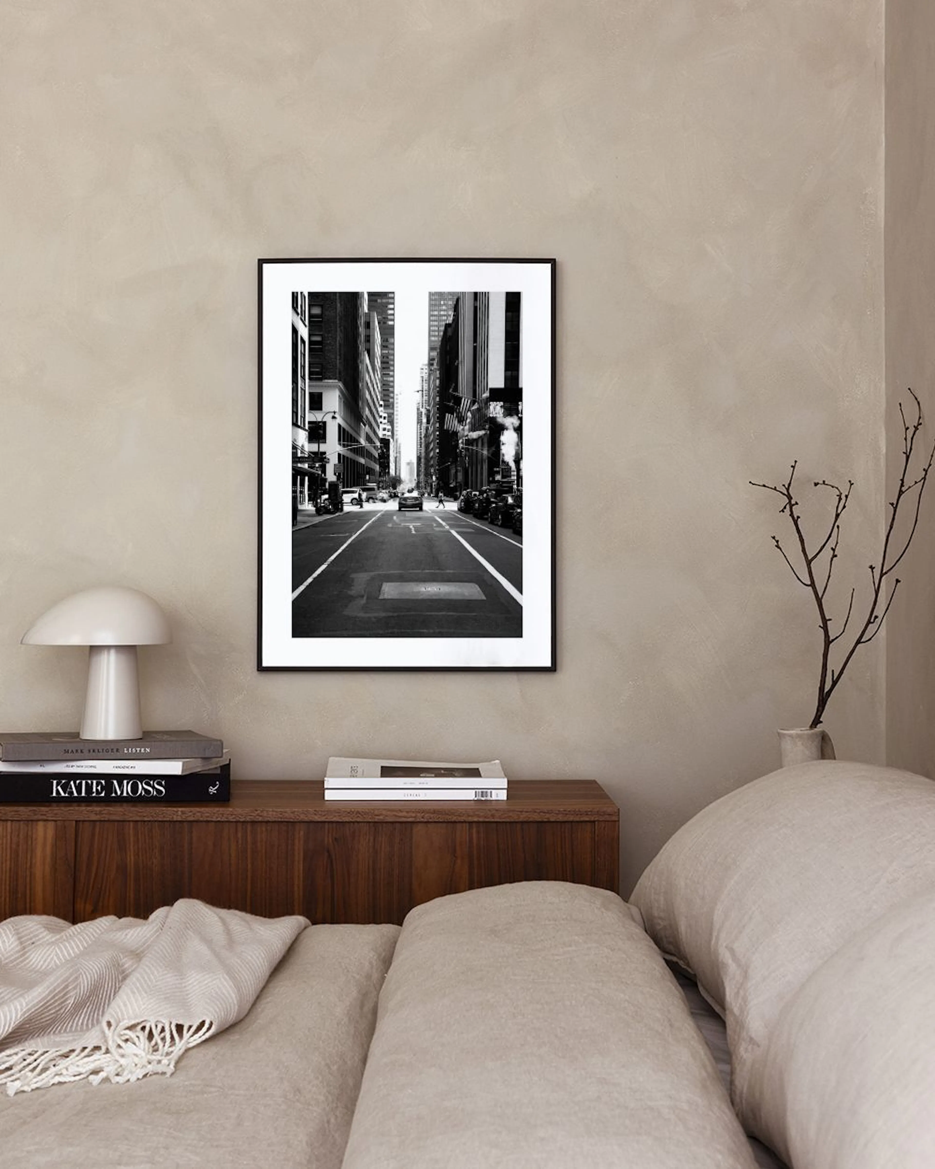 Zwart-wit poster van een New Yorkse straat met hoge gebouwen, hangend boven een zwart dressoir met boeken en decoratie.