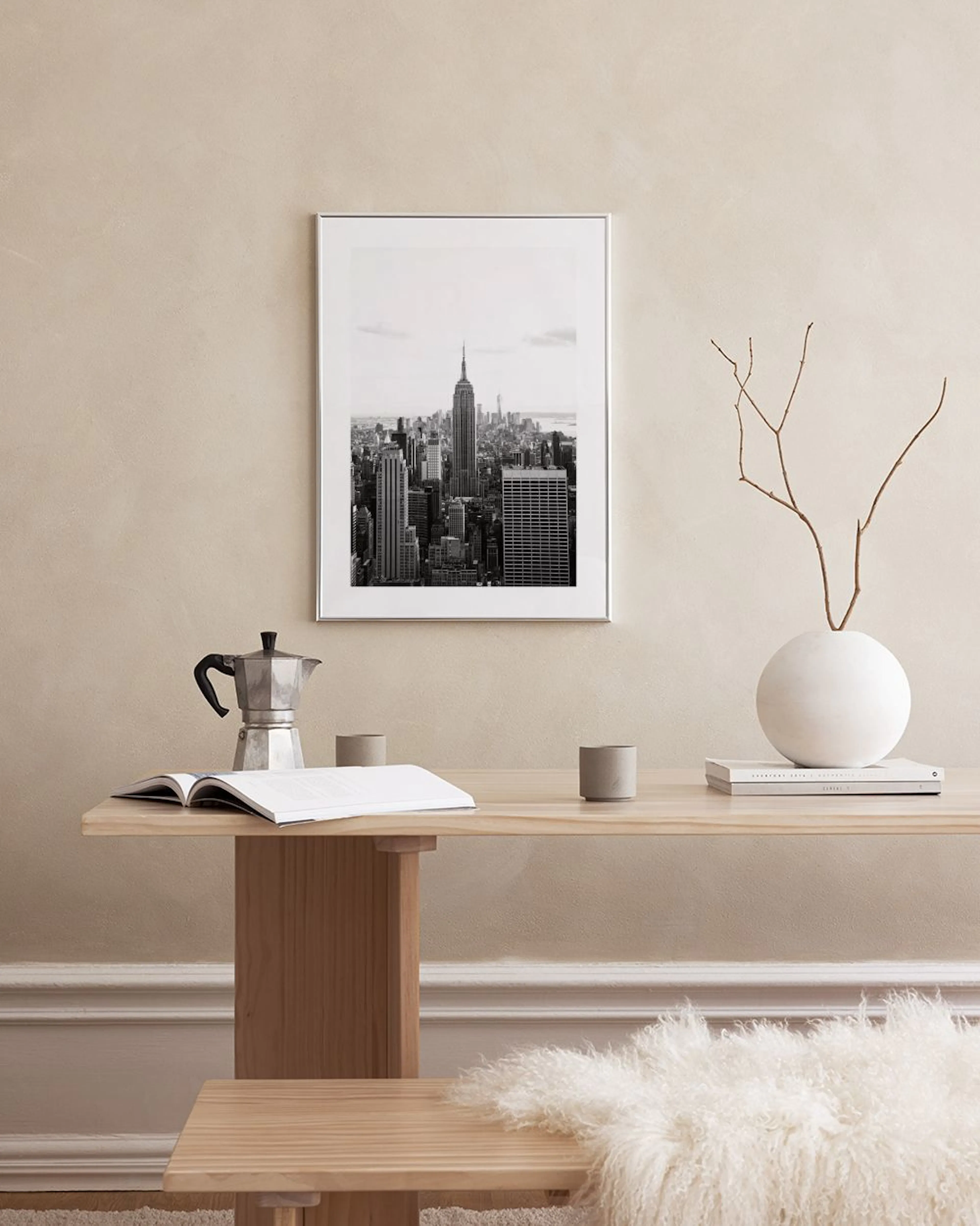 Zwart-wit poster van de skyline van New York City met het Empire State Building, hangend boven een wit dressoir met een vaas en 