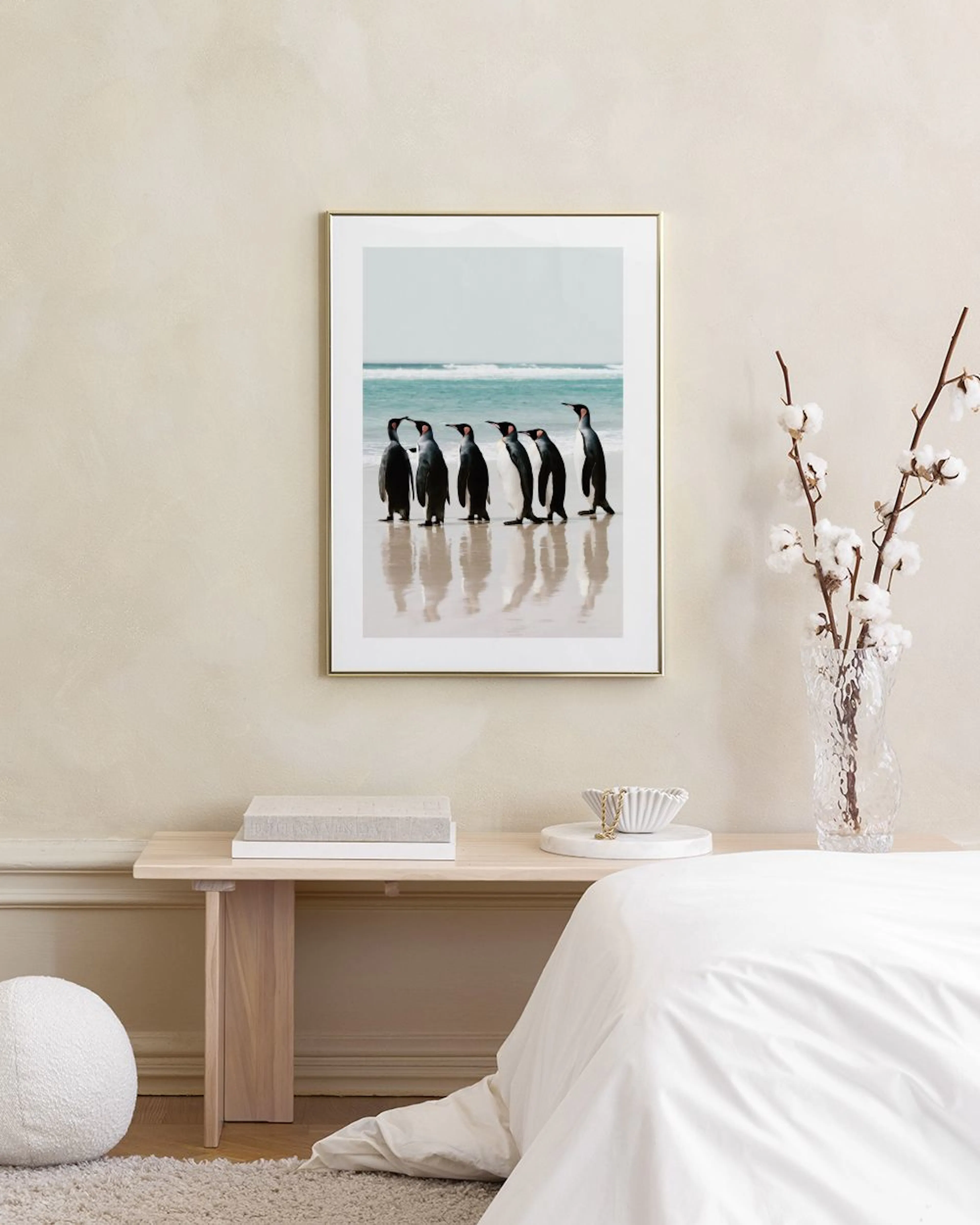 A print of six penguins walking on a wet beach with blue ocean waves, displayed above a blue cabinet with books and decor.
