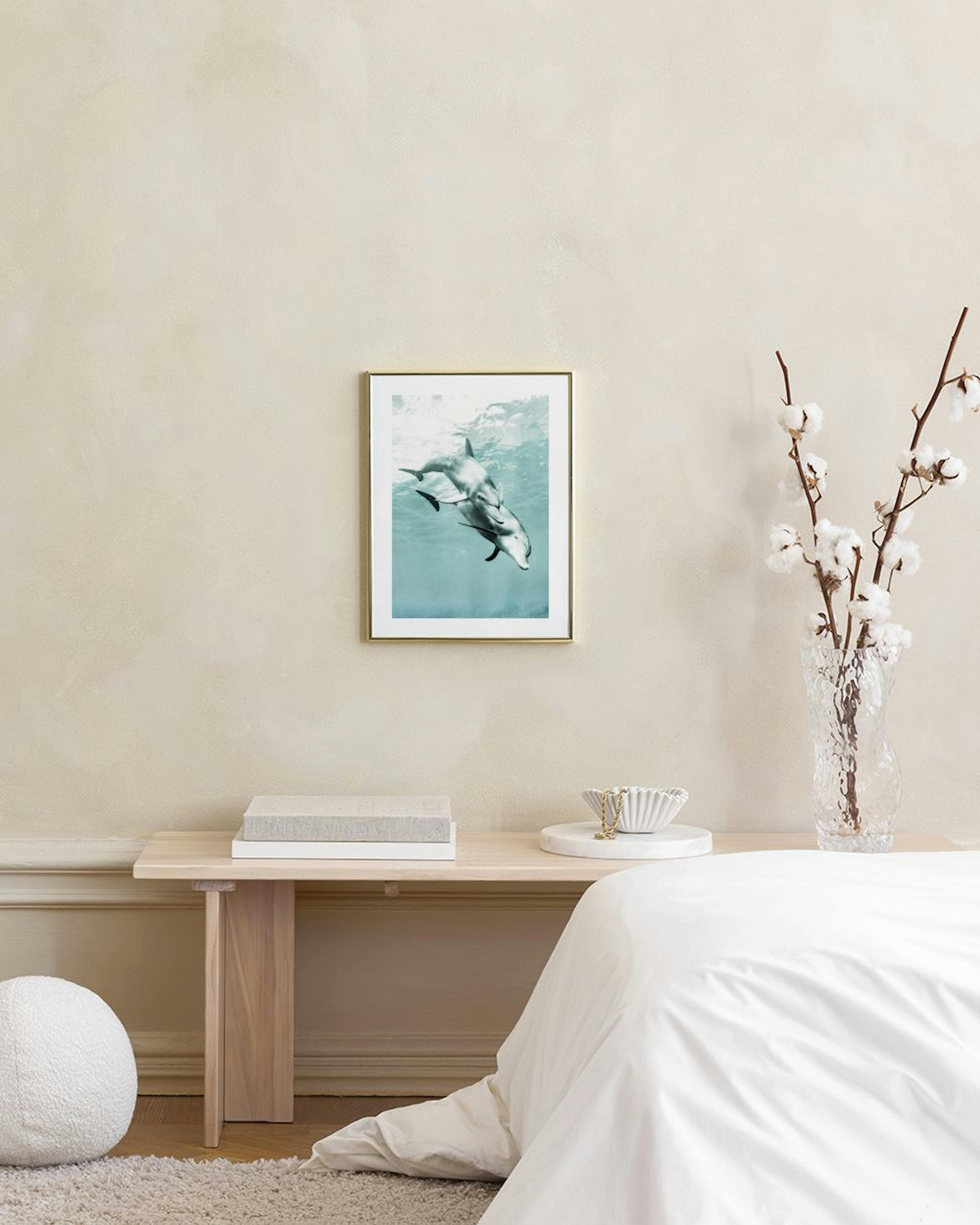 Plakat med to delfiner, der svømmer under vandet i turkisblåt hav, hængende over et hvidt marmorbord.