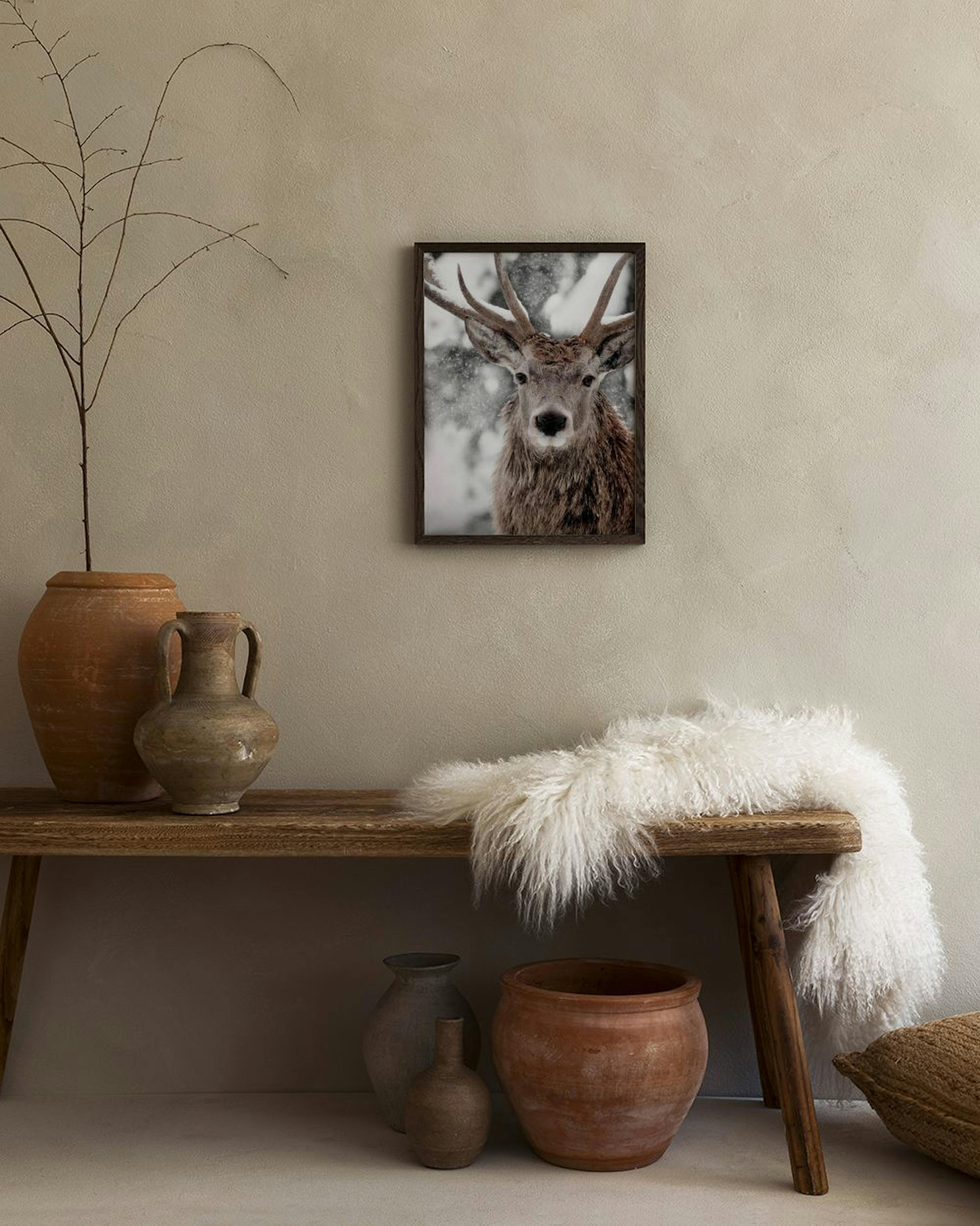 Affiche dun cerf aux bois majestueux sous la neige, accrochée au-dessus dune console grise avec livre et vase.