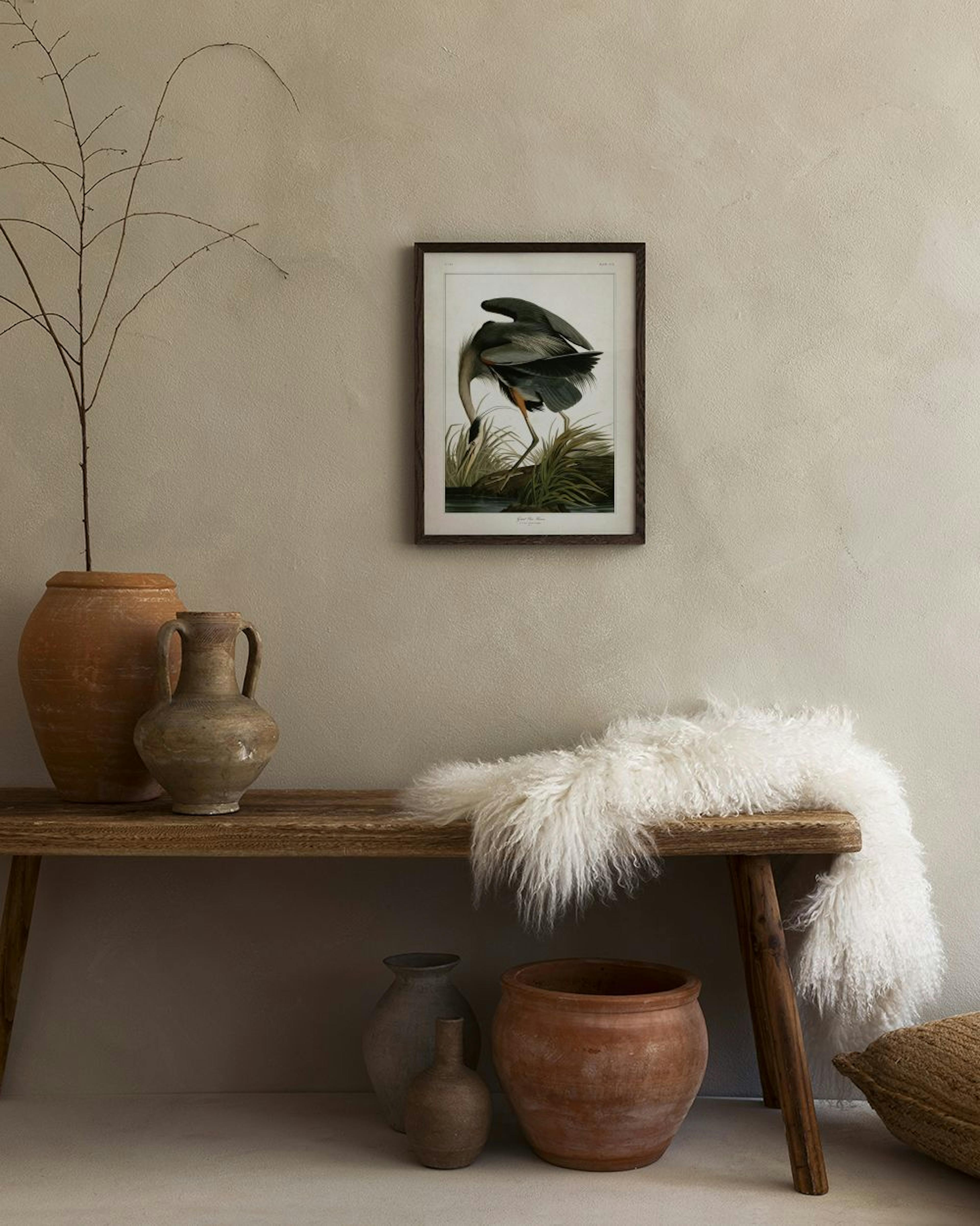 Plakat med illustration af en hejre i grå og sort farver, der søger føde i græsset ved vandet. Hænger i en moderne stue med en g