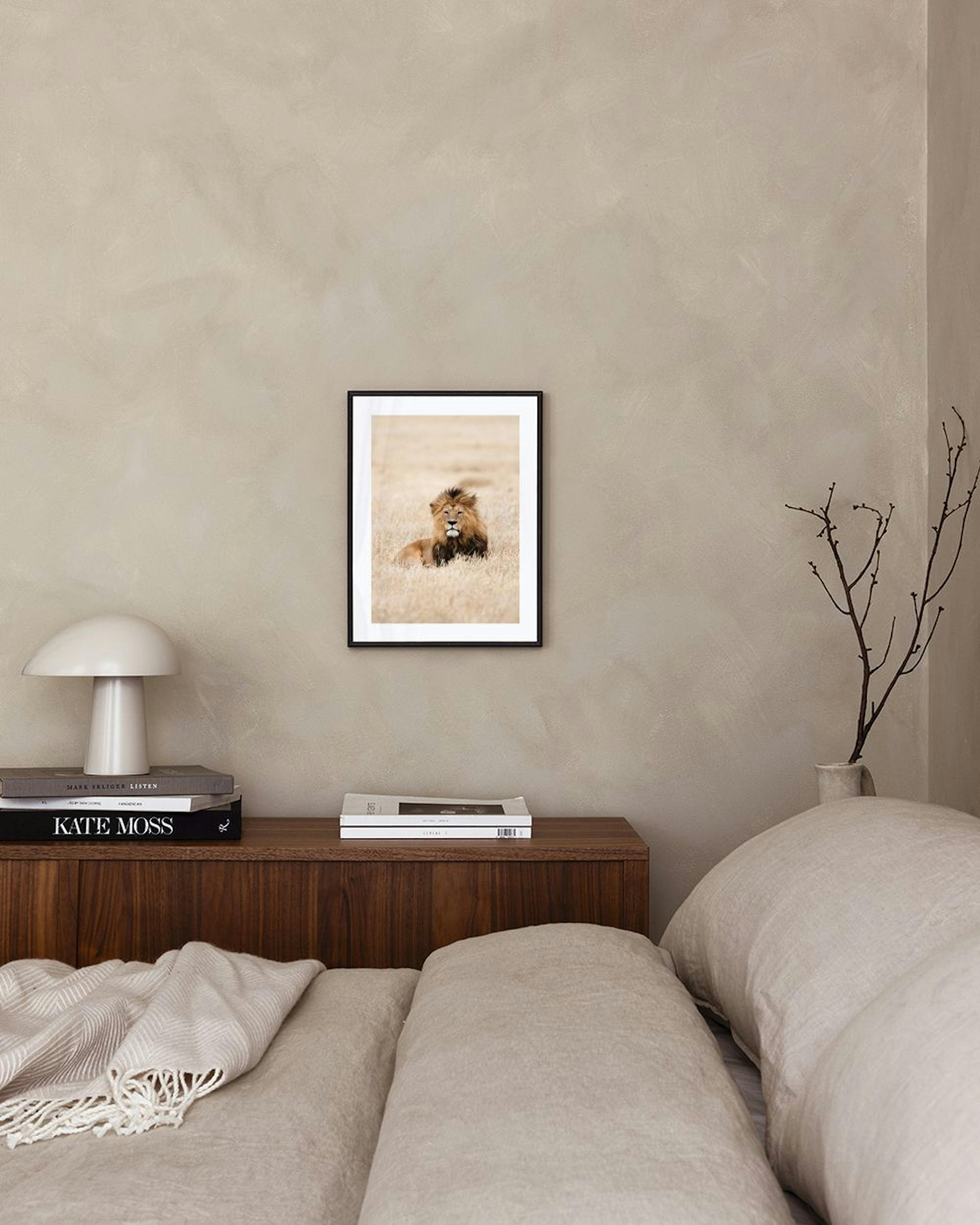 Affiche dun lion au repos dans lherbe sèche, affichée au-dessus dun meuble gris avec une lampe et des livres.