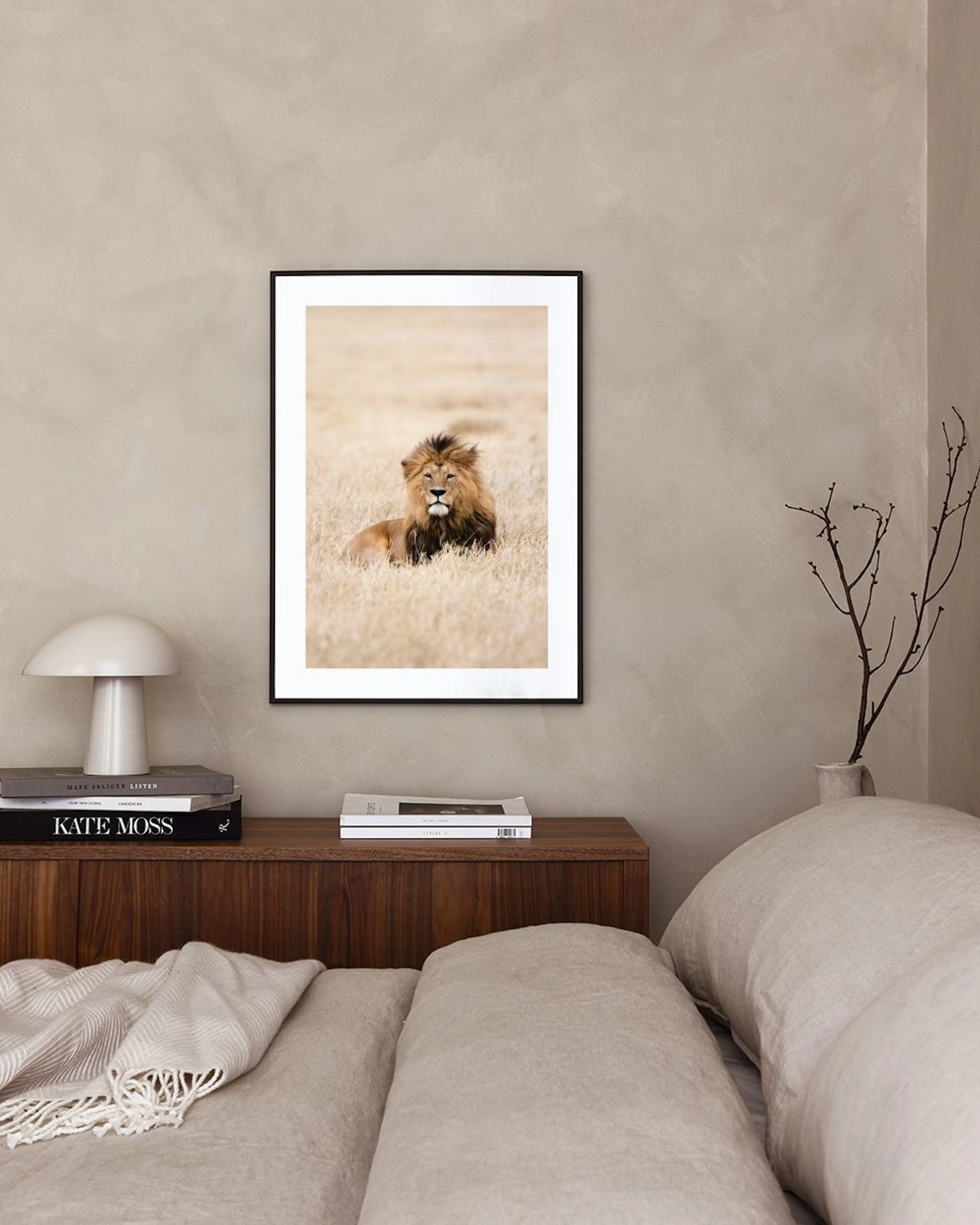 Affiche dun lion au repos dans lherbe sèche, affichée au-dessus dun meuble gris avec une lampe et des livres.