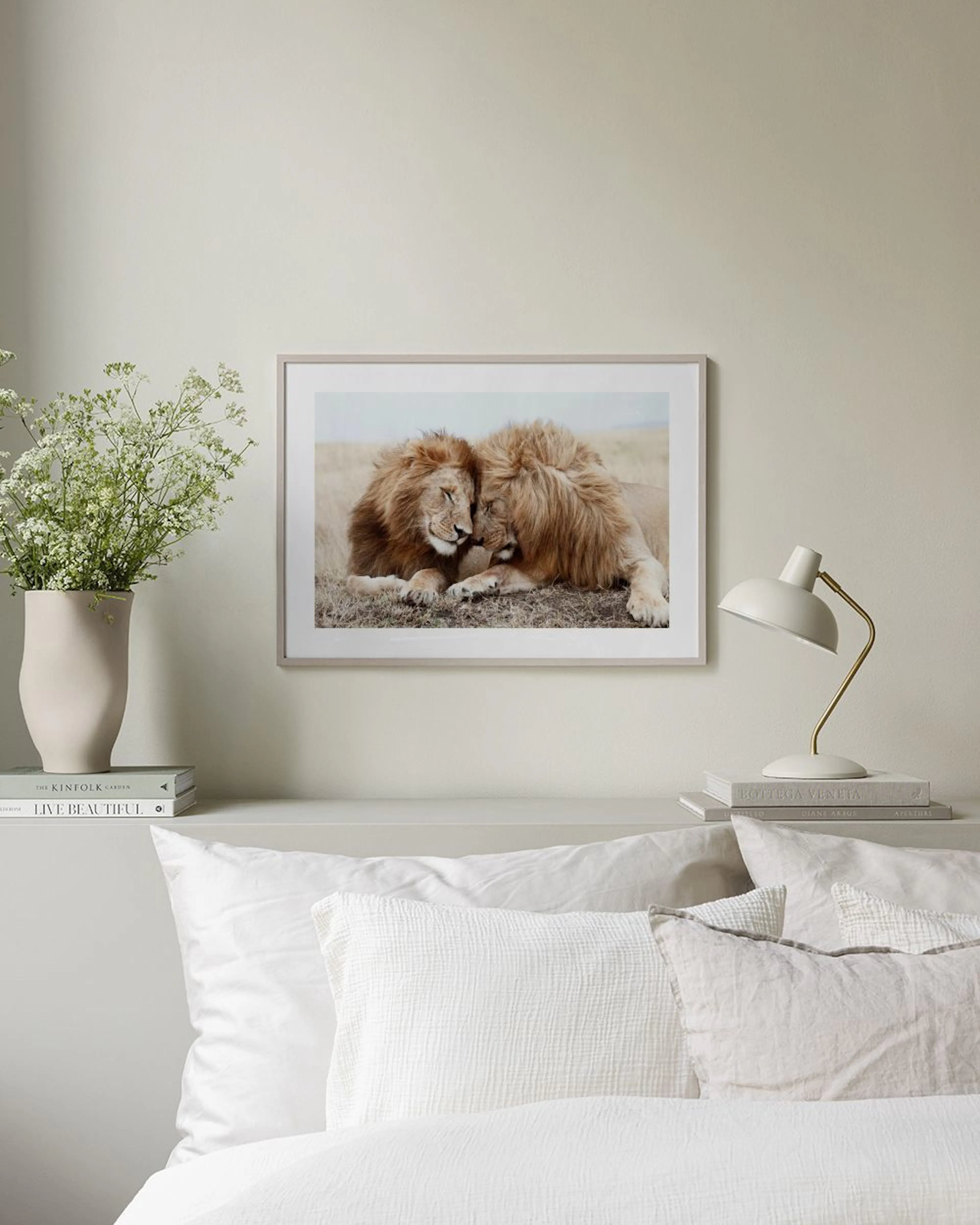 A print of two majestic lions resting together in a field, displayed on a wooden cabinet with a lamp and vase.