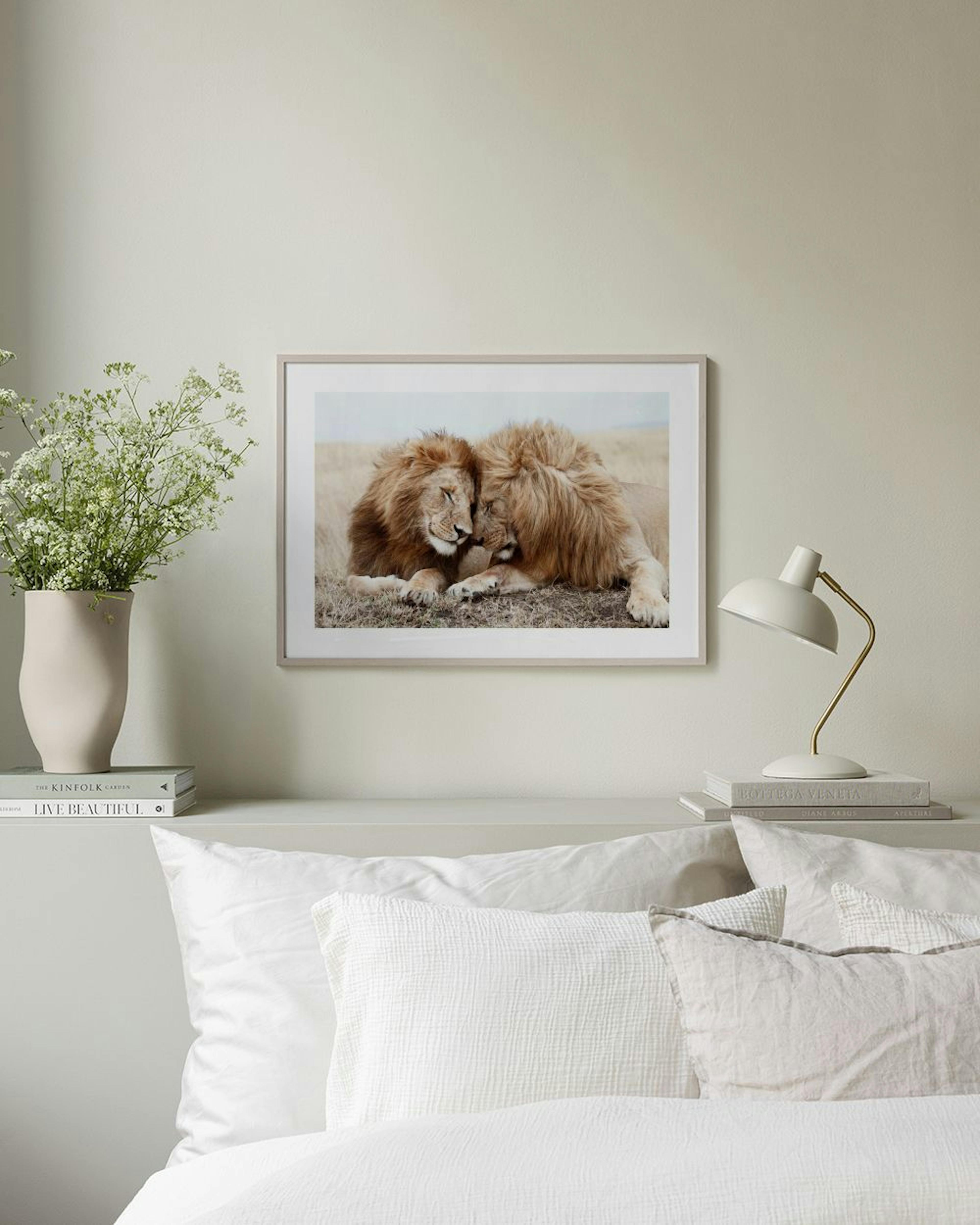 A print of two lions nuzzling, lying in dry grass, displayed on a wooden cabinet with a white lamp and vase.
