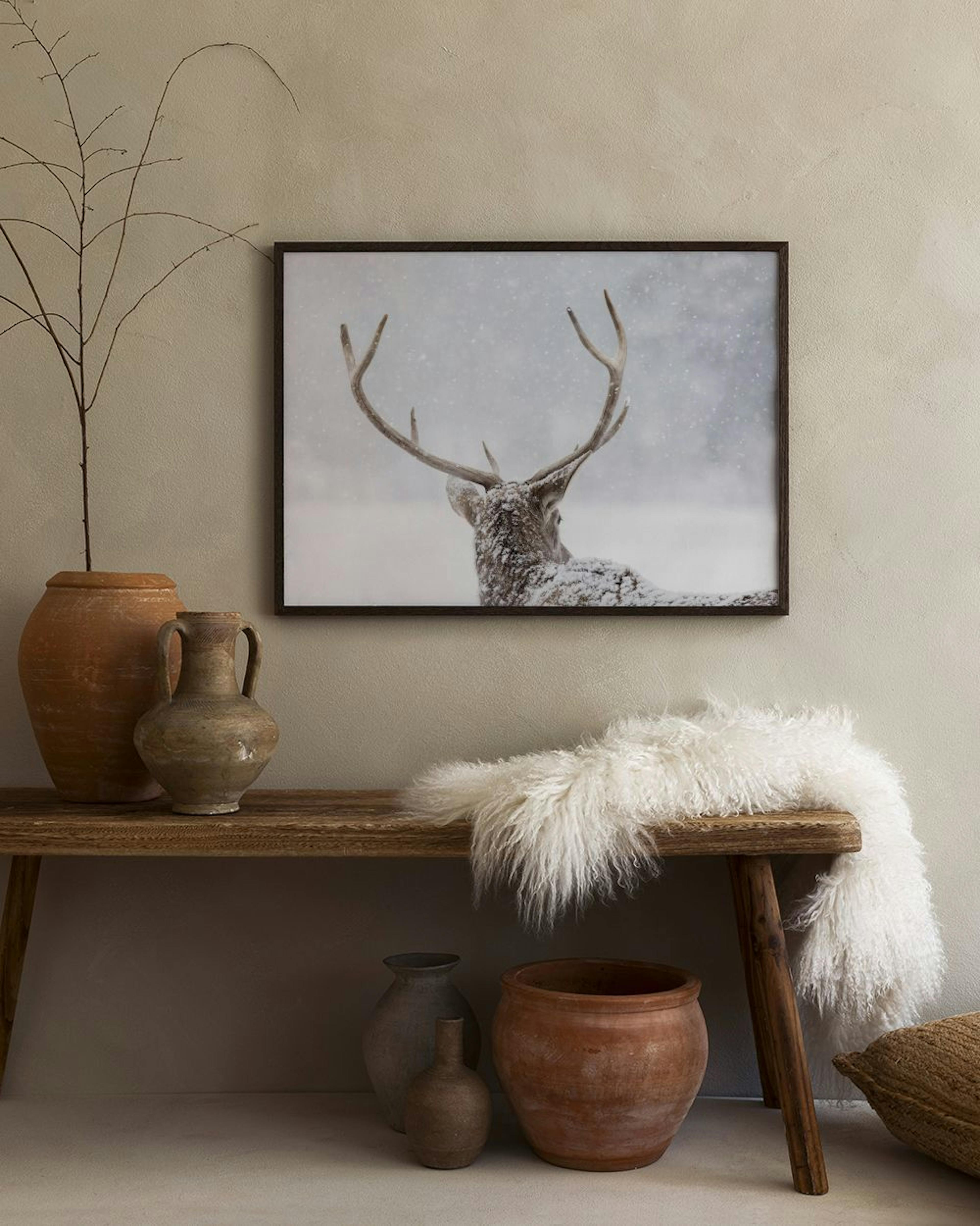 Affiche dun cerf enneigé en hiver, accrochée au mur clair dun salon moderne avec une chaise grise et une table basse.