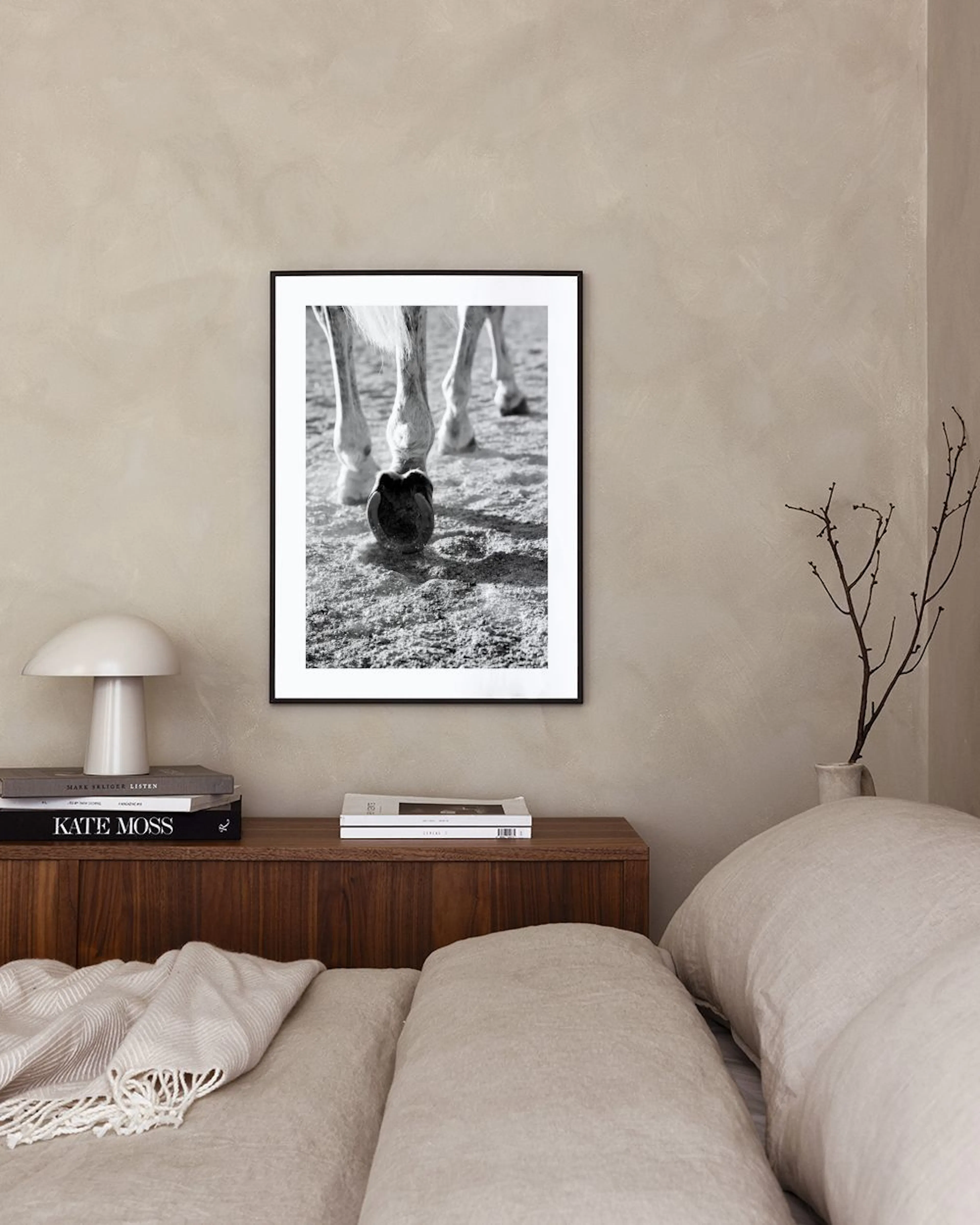 A black and white print of a horses legs and hooves standing on dusty ground, displayed in a room above a brown leather butterfl
