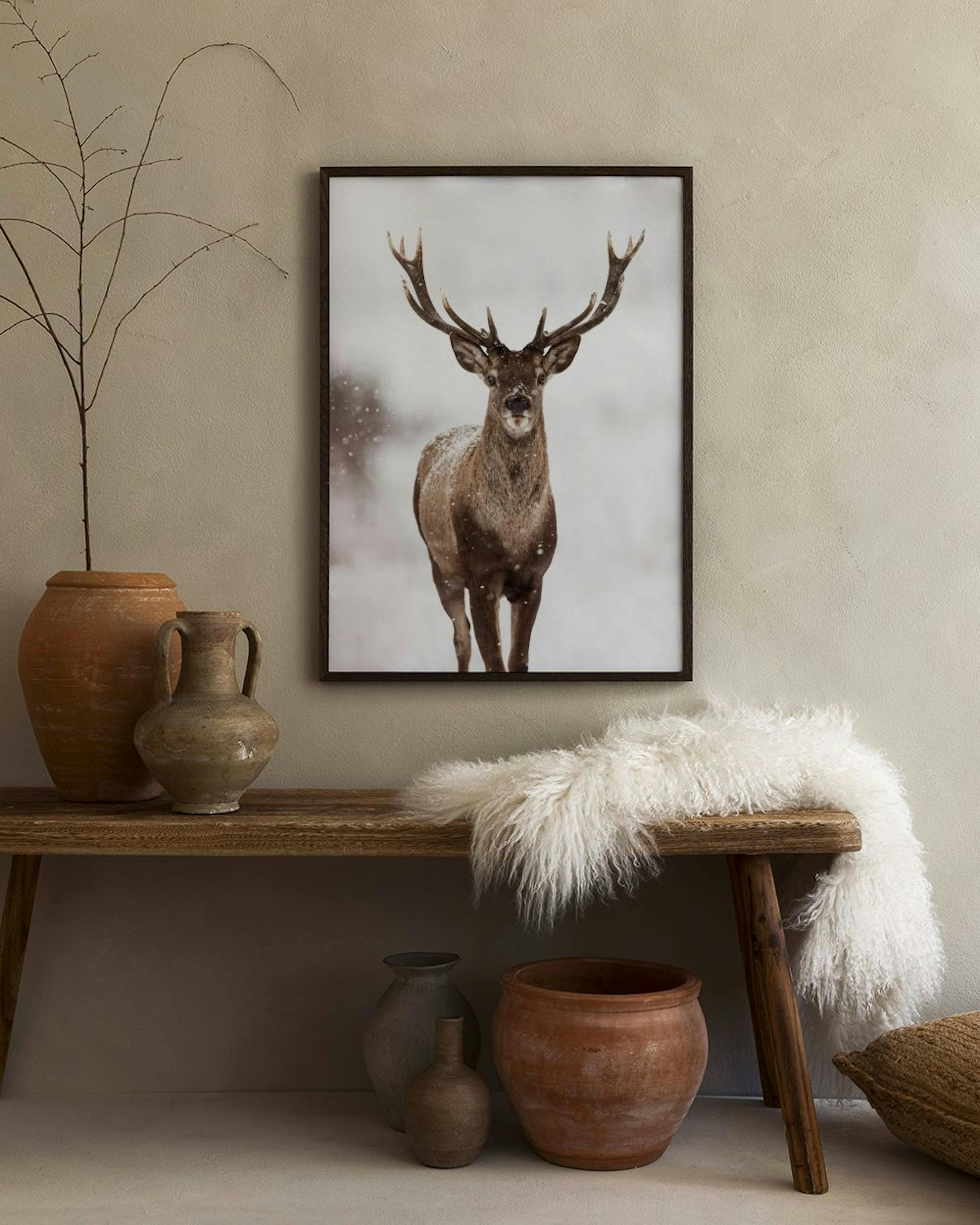 Poster eines Hirschs im Schnee, gerahmt an einer weißen Wand über einem weißen Sideboard mit grauer Vase und Ledersessel.