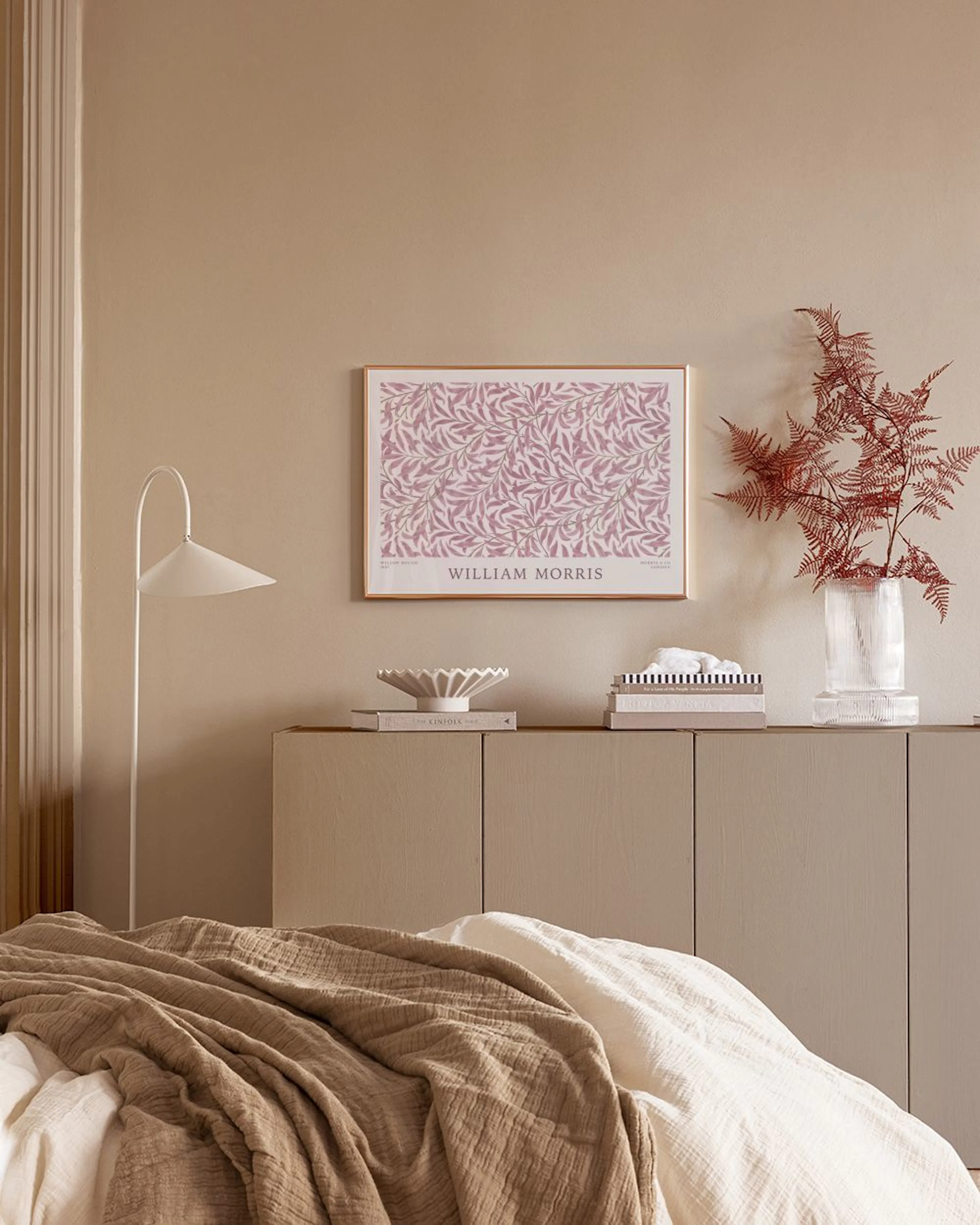 Poster med rosa lövmönster av William Morris i ett sovrum med säng och sängbord.