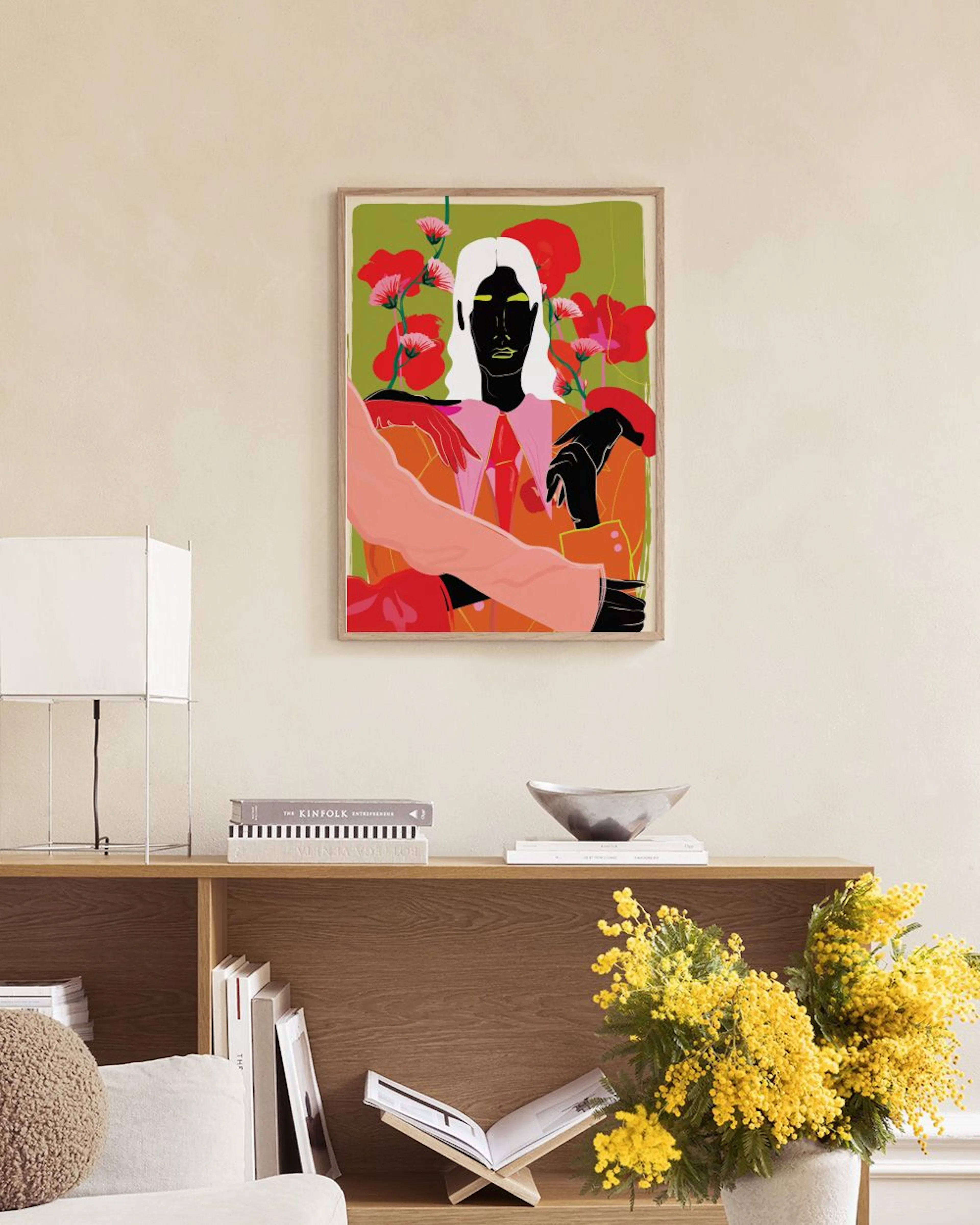 Plakat med en person i rosa jakke og slips, omgitt av store røde blomster på grønn bakgrunn, henger i en moderne stue over et bo