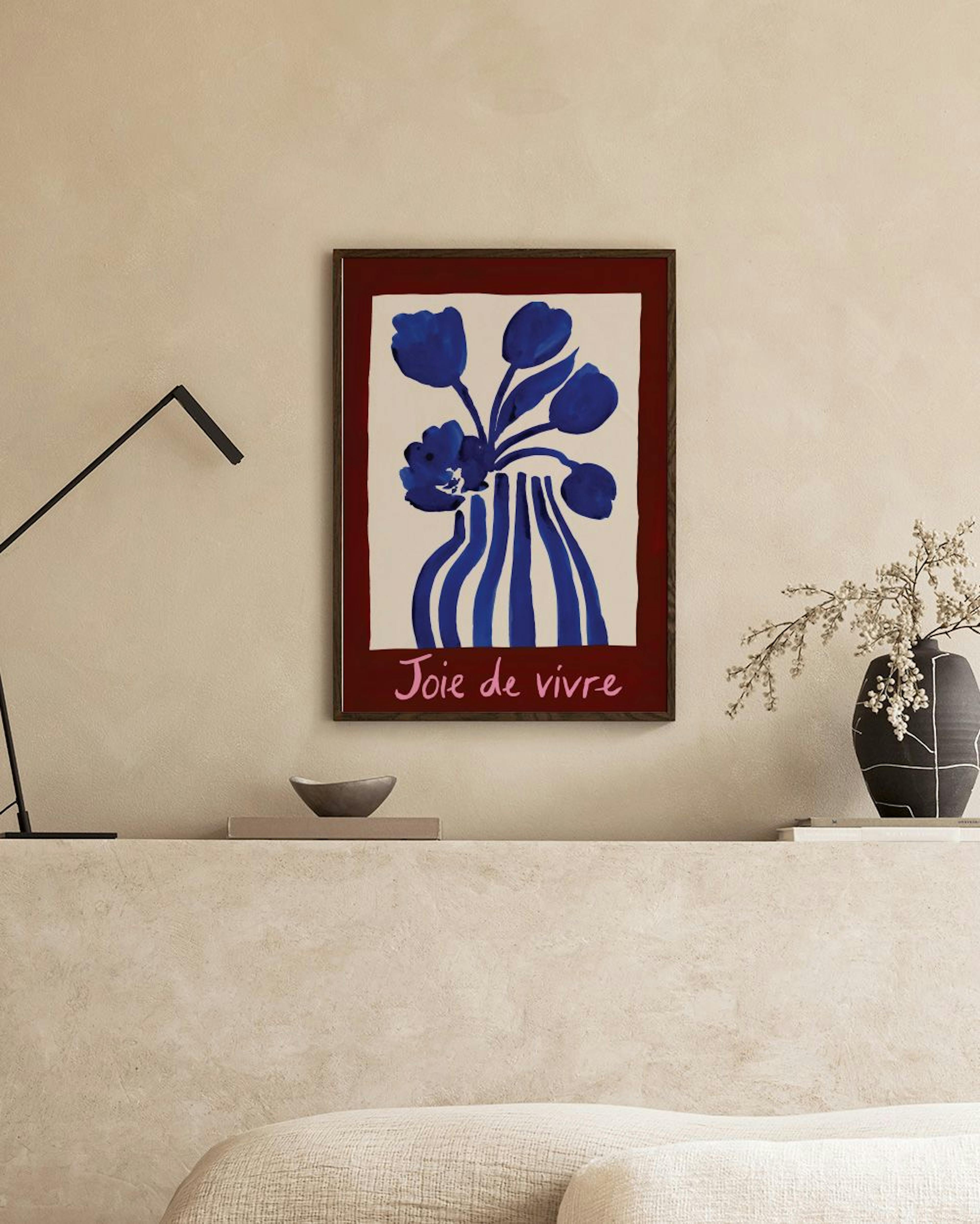 Poster mit blauen Blumen in gestreifter Vase, umgeben von einem dunkelroten Rand, hängt über einem Sofa.