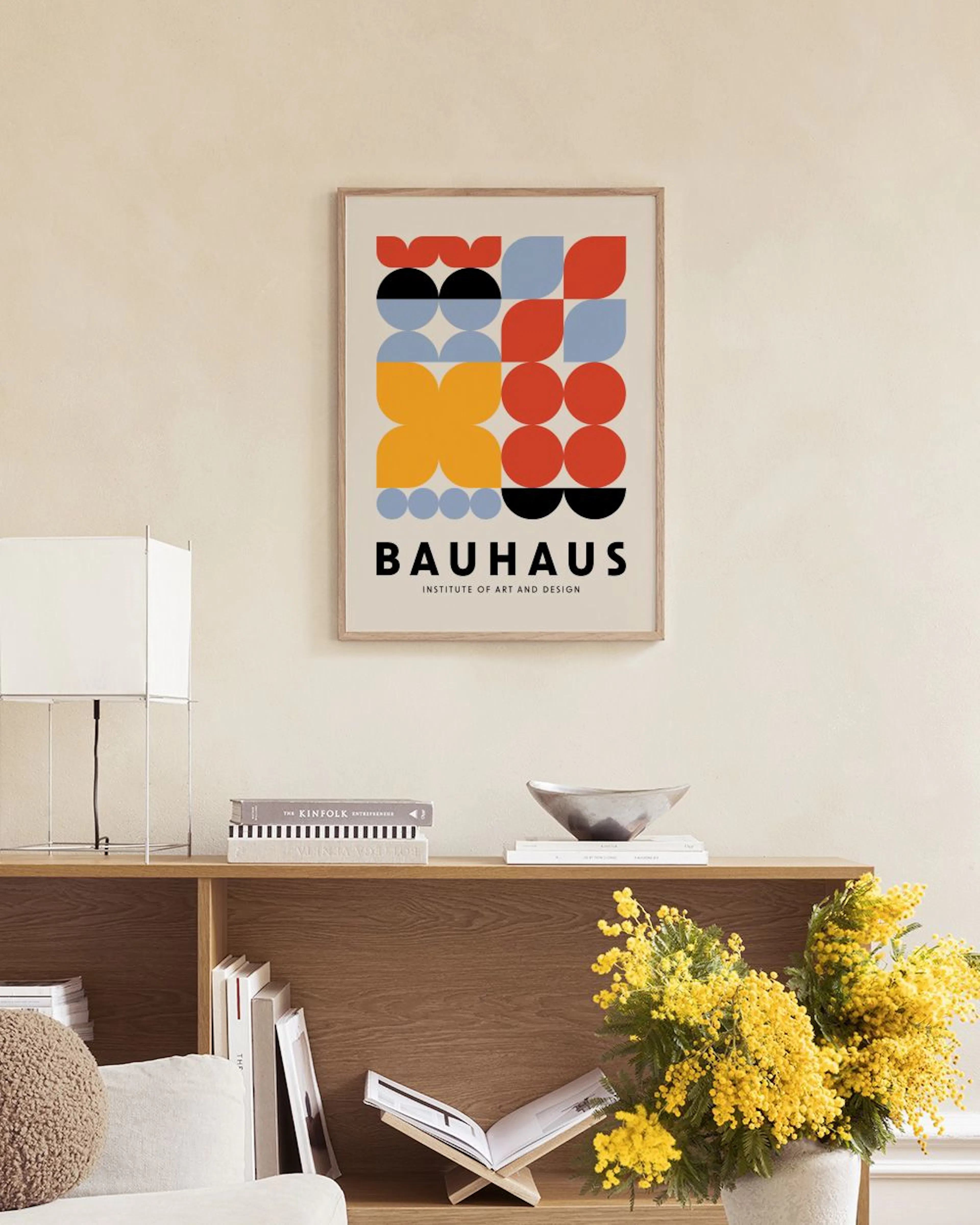 A Bauhaus print with red, blue, yellow, and black geometric shapes, displayed above a wooden bench with pottery.
