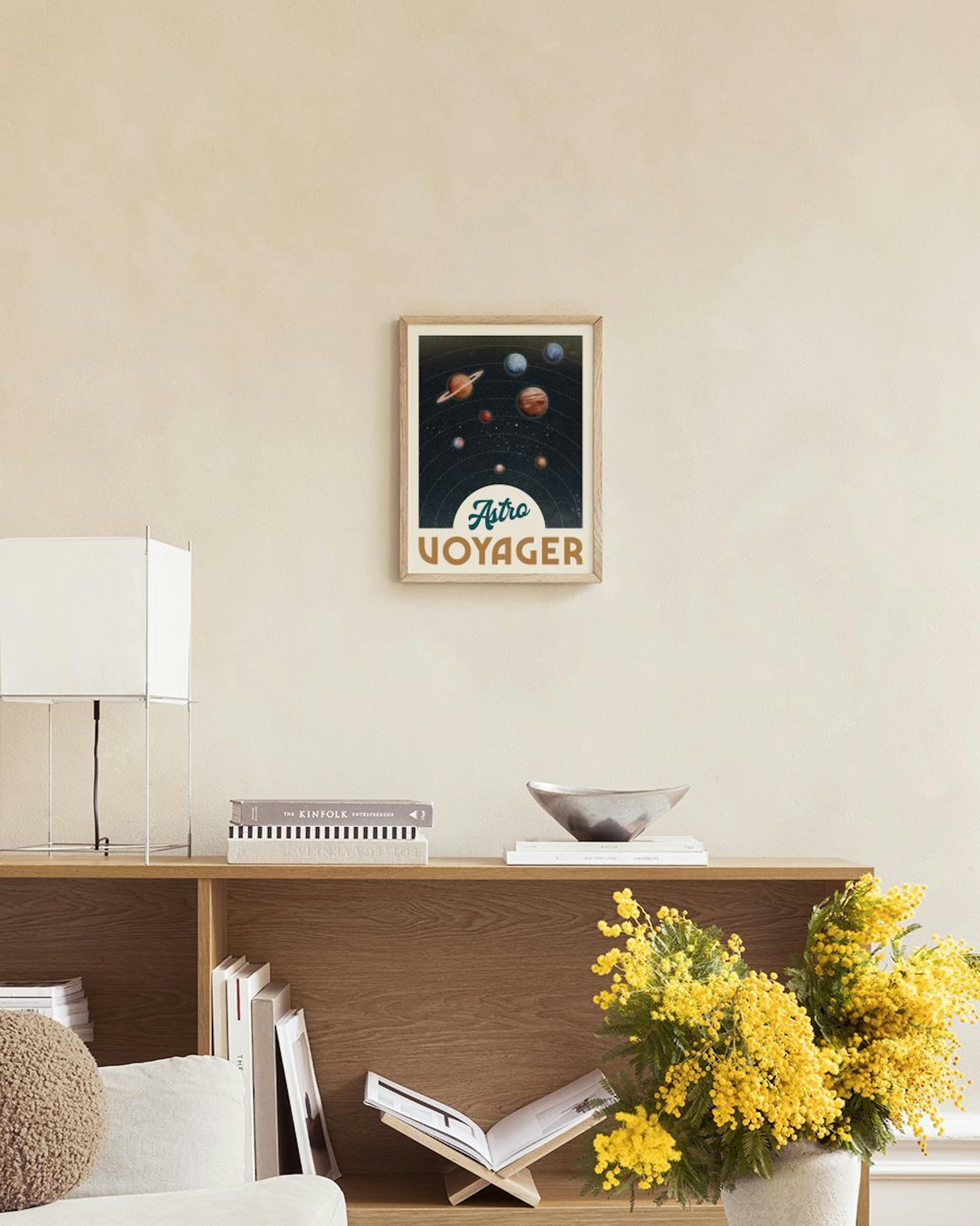 A vintage solar system print with planets and the words Astro Voyager, hanging on a white wall above a grey table and ottoman.