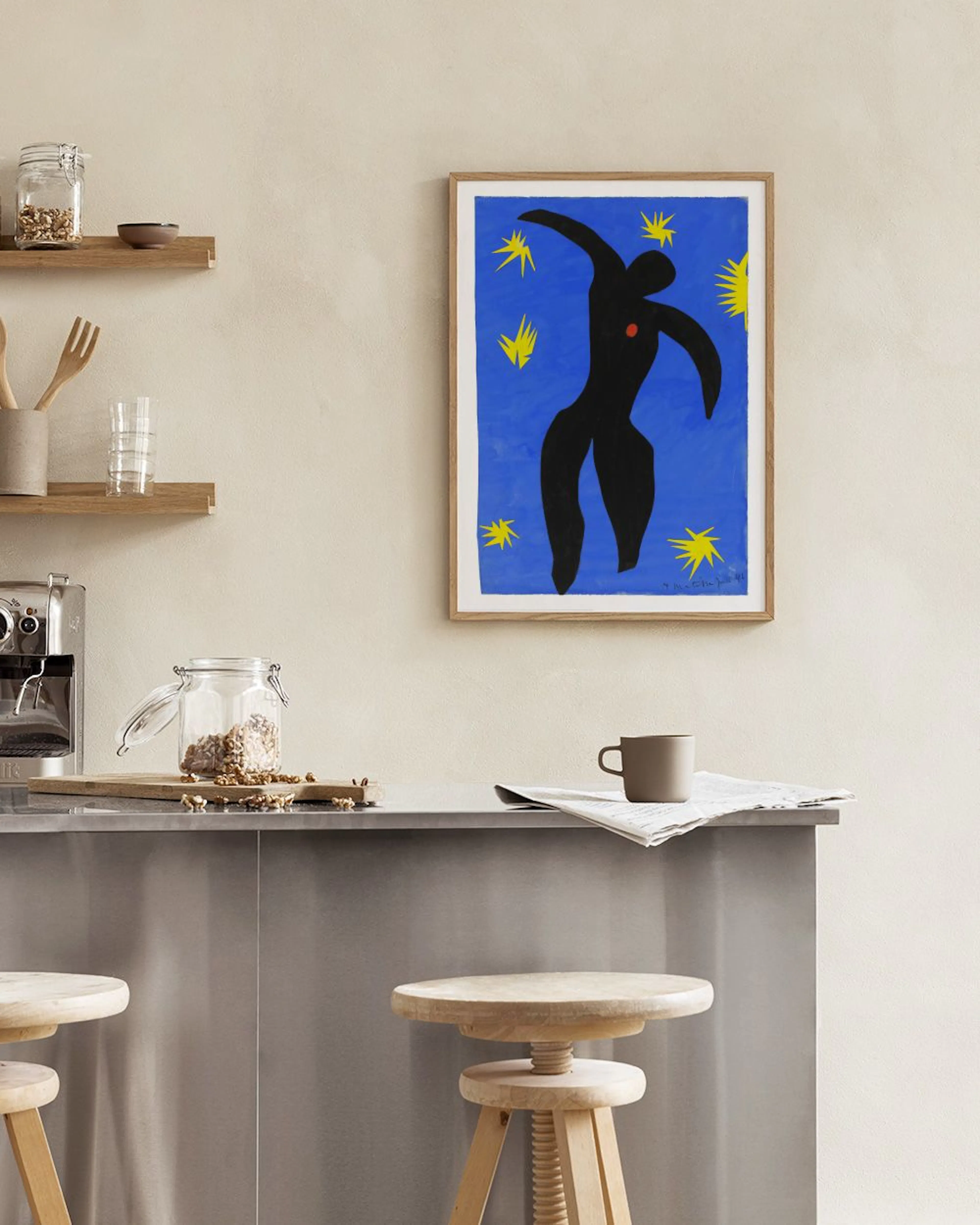 Poster con figura astratta nera e stelle gialle su sfondo blu, appeso in una stanza moderna sopra una poltrona neutra.