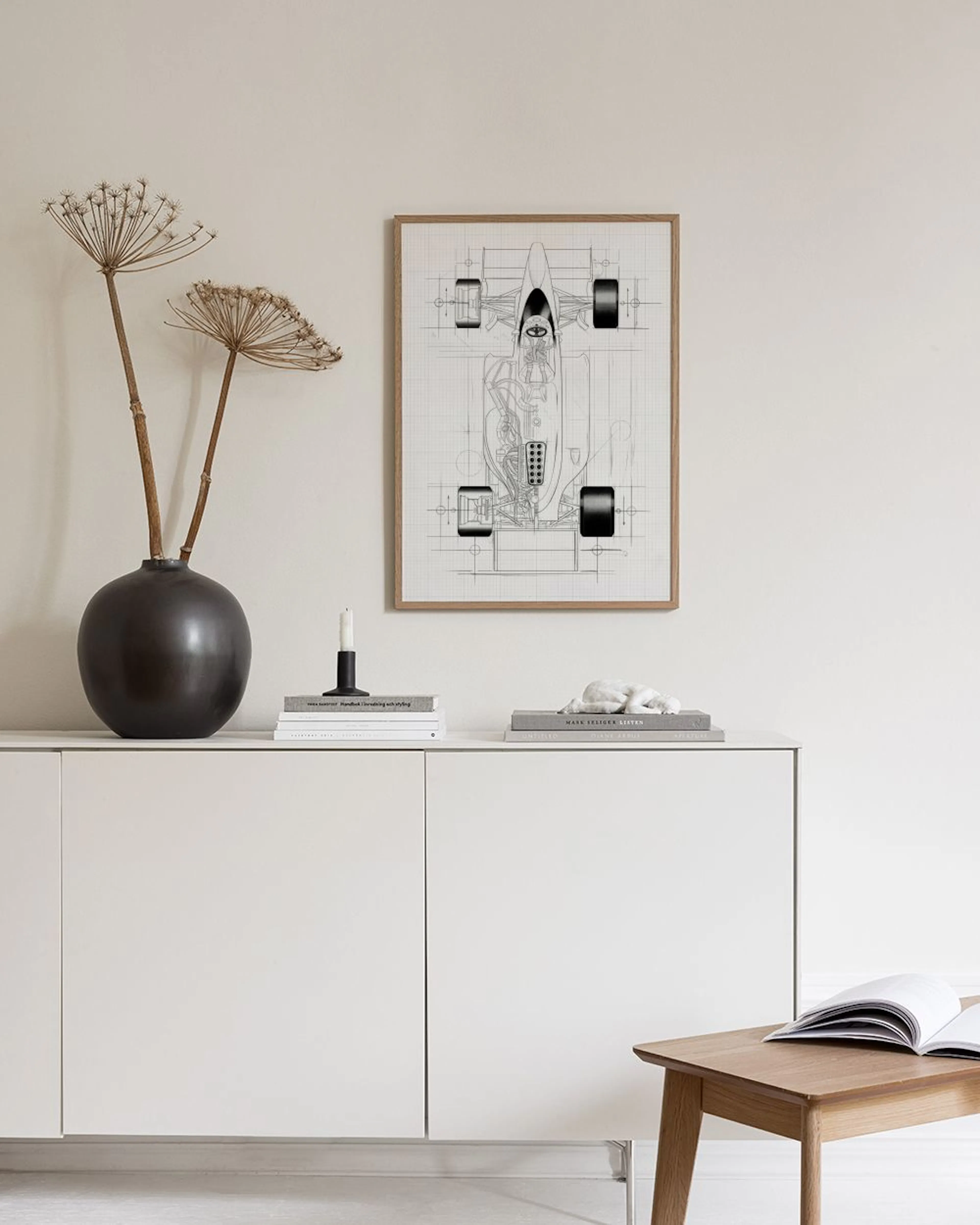 A detailed black and white blueprint of a Formula 1 car, hanging on a white wall above a neutral armchair.