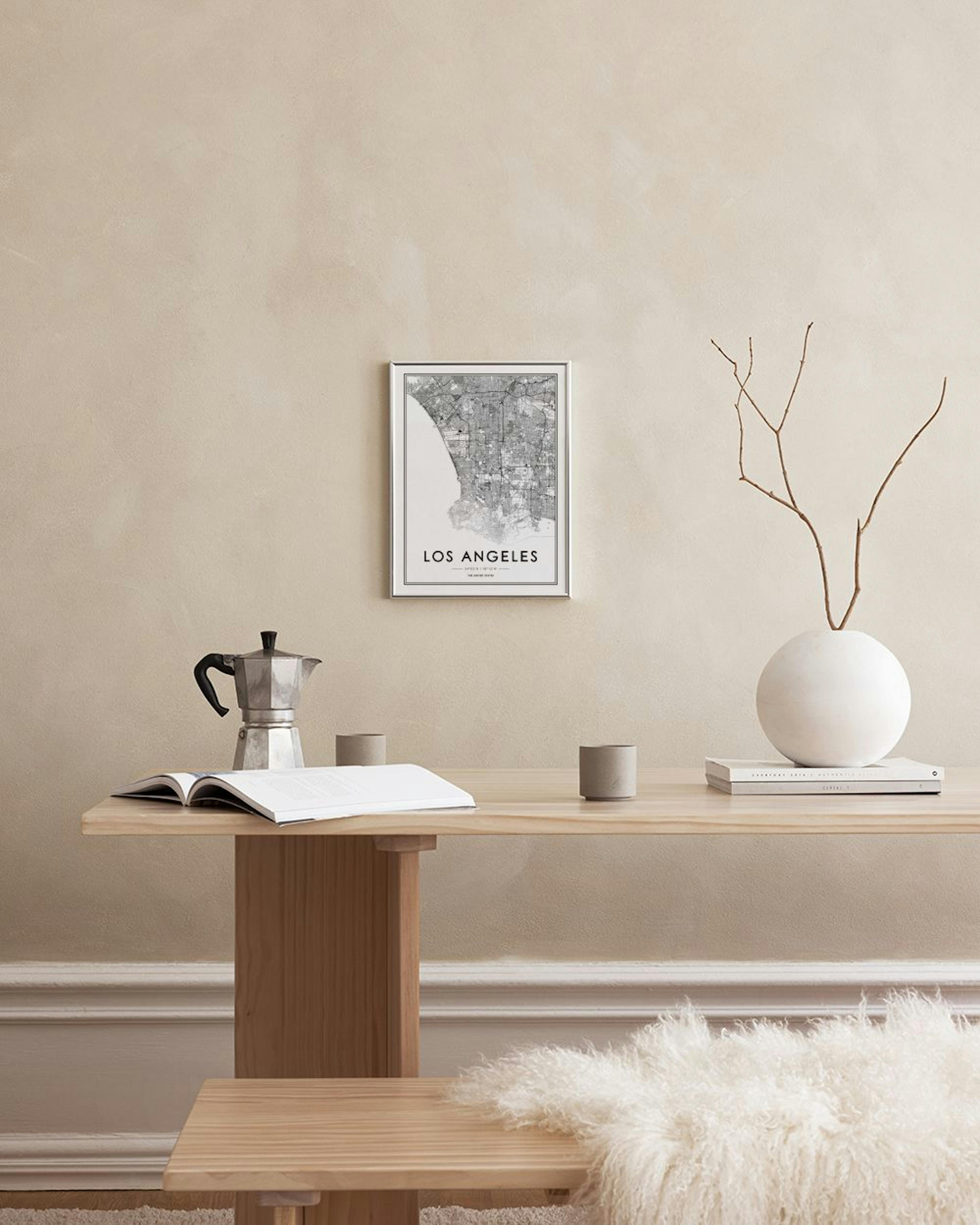 A Los Angeles map print hangs on a black grid, above a woven basket with eucalyptus, vases, and a chair with a blanket.